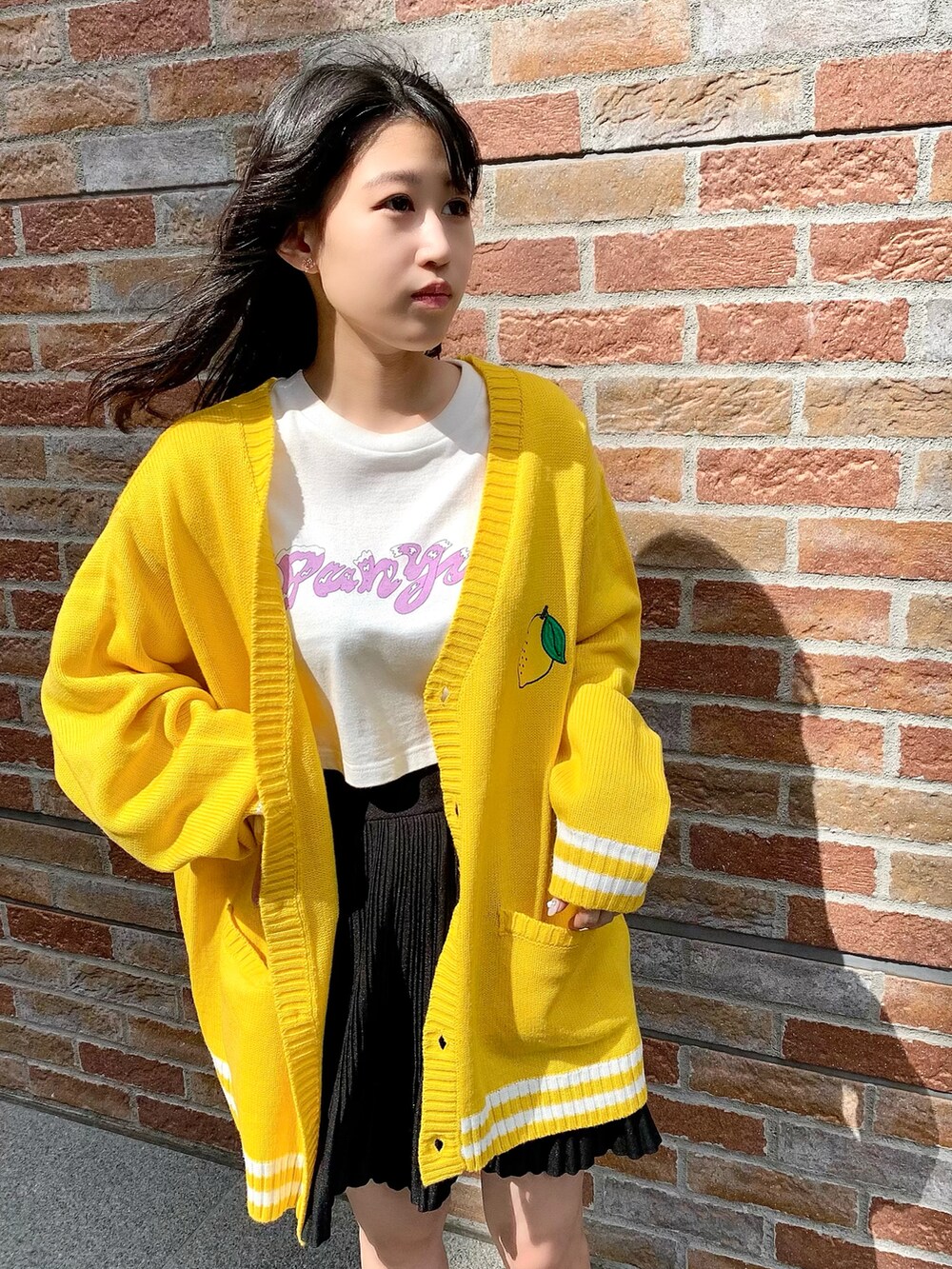 ブラック系のスカート、ホワイト系のTシャツ/カットソー、イエロー系のカーディガン/ボレロを着用したレディースの夏コーディネートの2枚目の写真