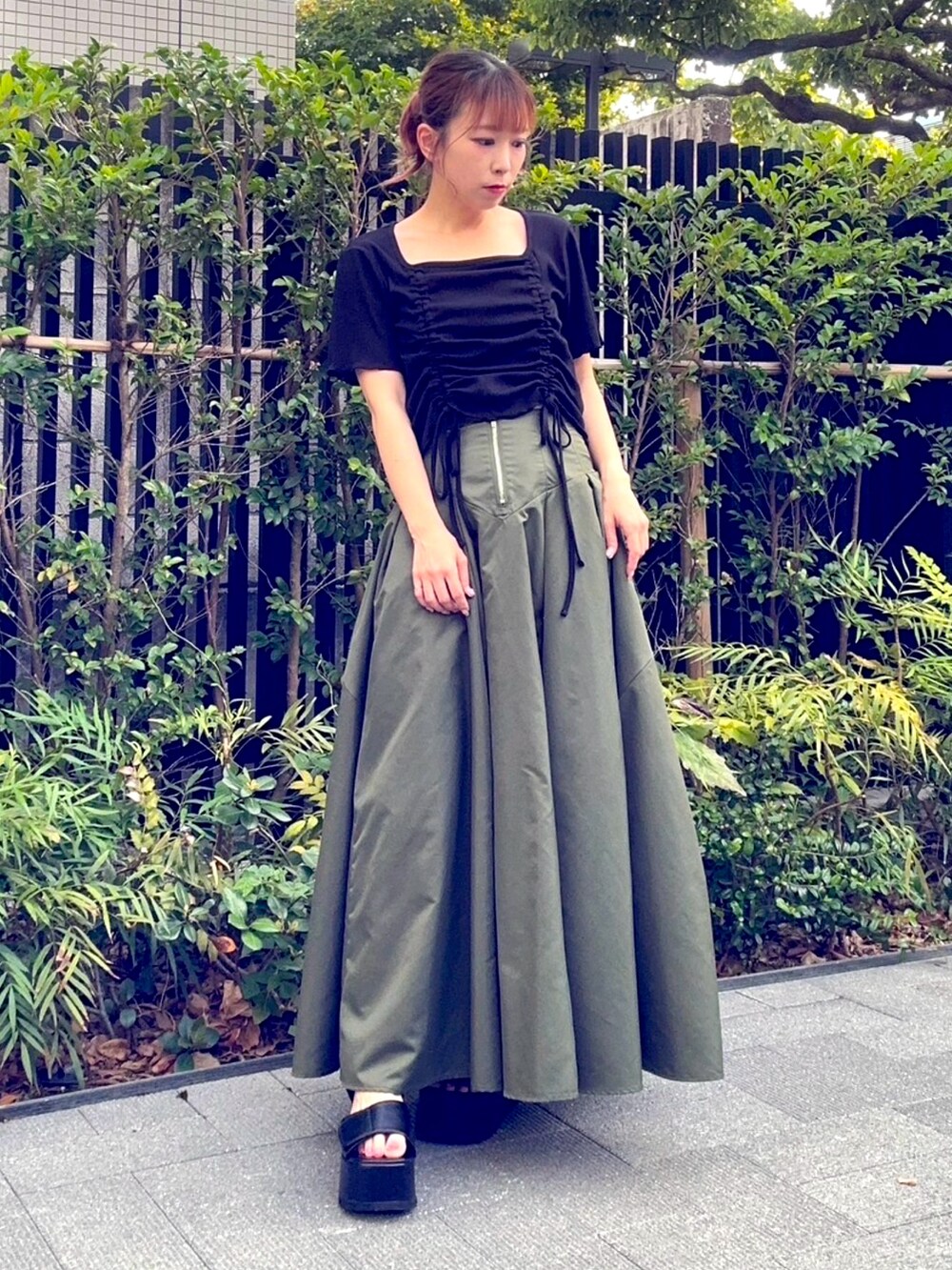 グリーン系のスカート、ブラック系のTシャツ/カットソーを着用したレディースの夏コーディネートの2枚目の写真
