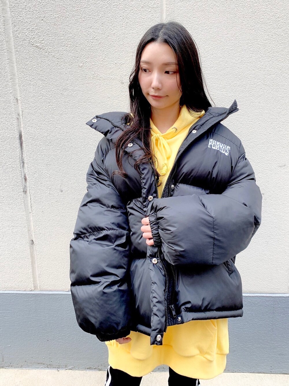 イエロー系のパーカー、ブラック系のダウンジャケット/コート、ホワイト系のレギンス/スパッツを着用したレディースの冬コーディネートの2枚目の写真