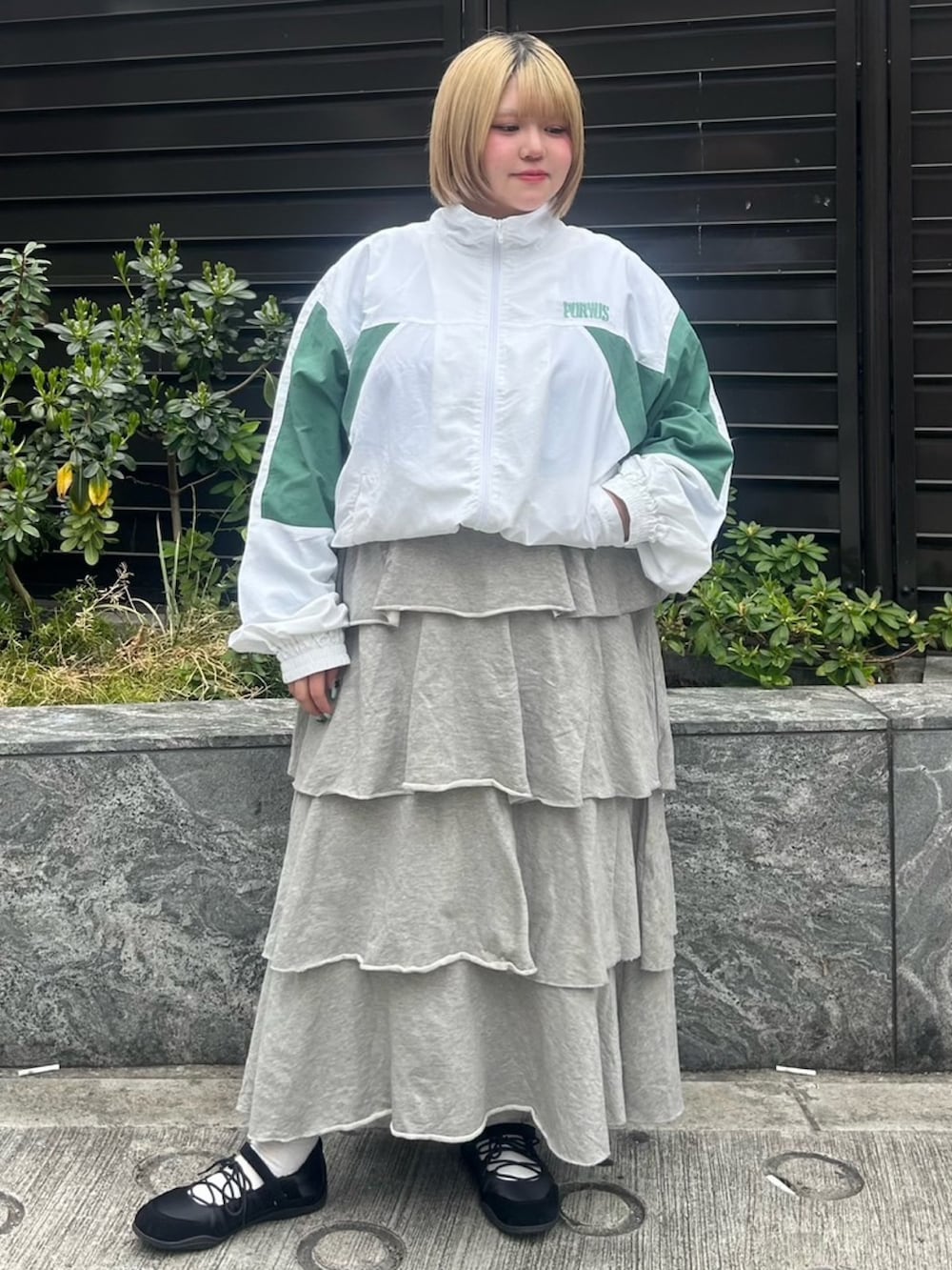 グレー系のスカート、ホワイト系のナイロンジャケットを着用したレディースの春コーディネートの2枚目の写真