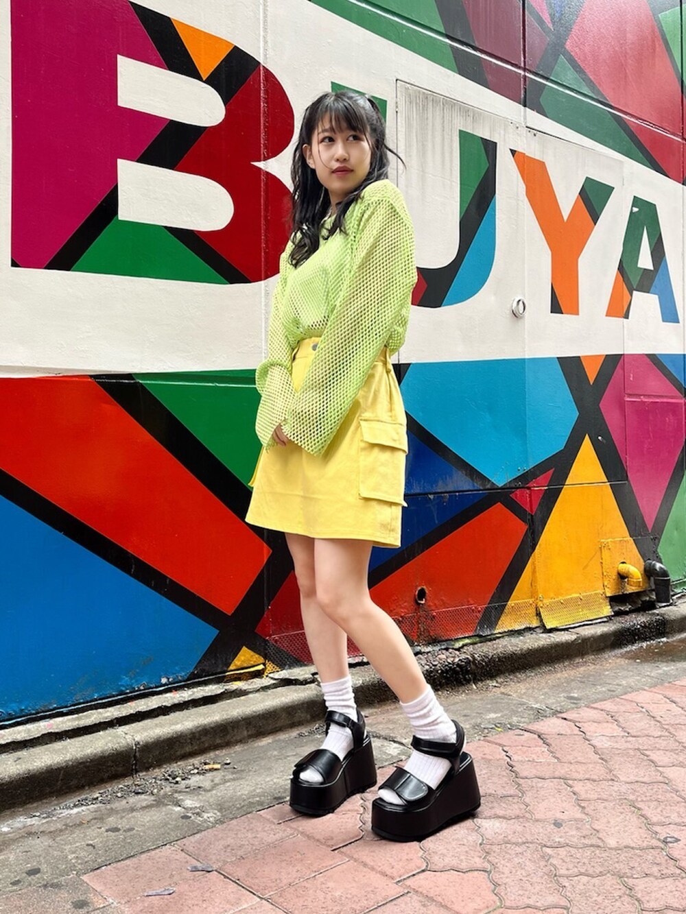 ブラック系のサンダル、グリーン系のTシャツ/カットソー、イエロー系のスカートを着用したレディースの夏コーディネートの2枚目の写真