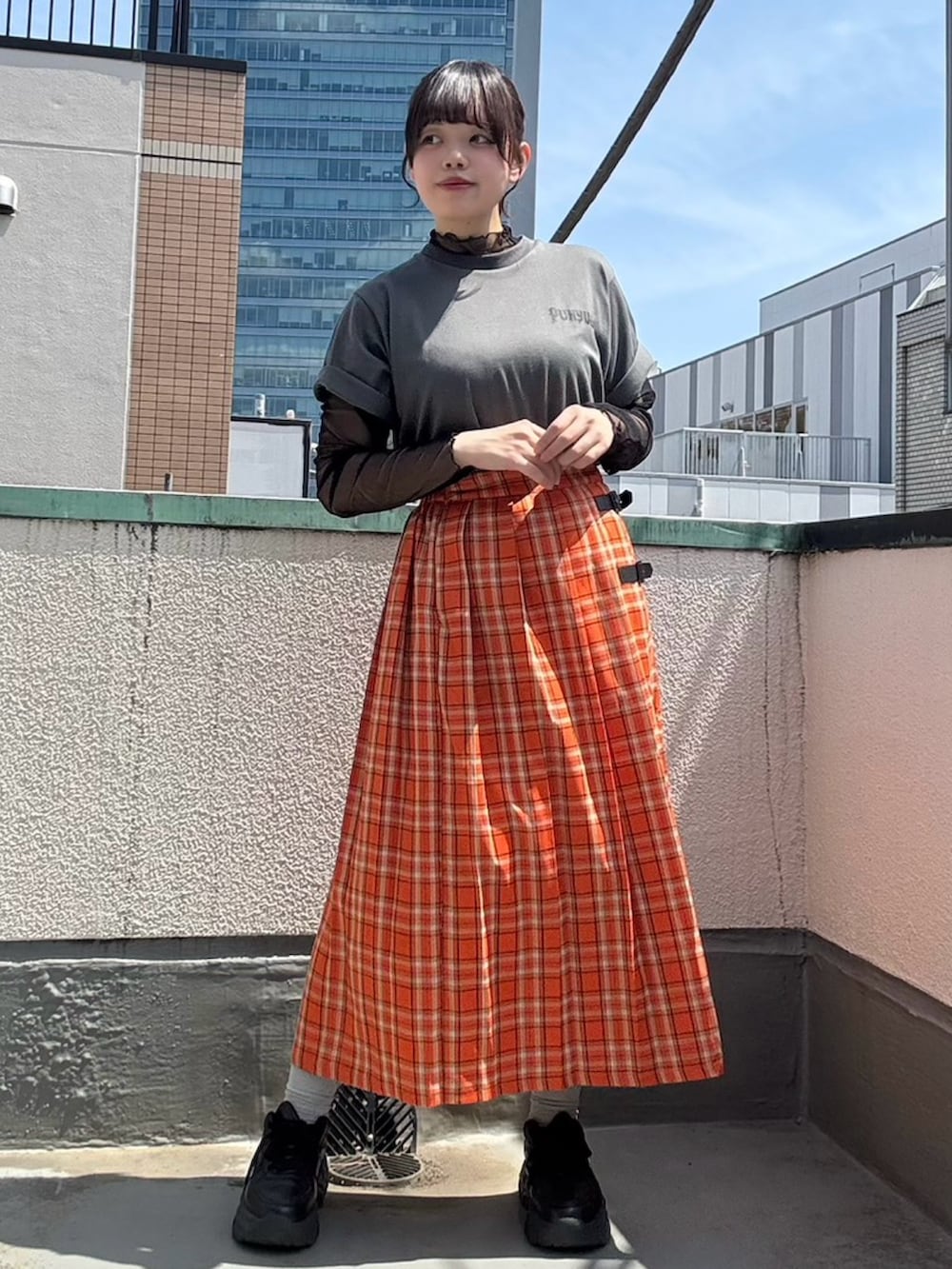 オレンジ系のスカート、ブラック系のTシャツ/カットソー、ブラック系のTシャツ/カットソーを着用したレディースの春コーディネートの2枚目の写真