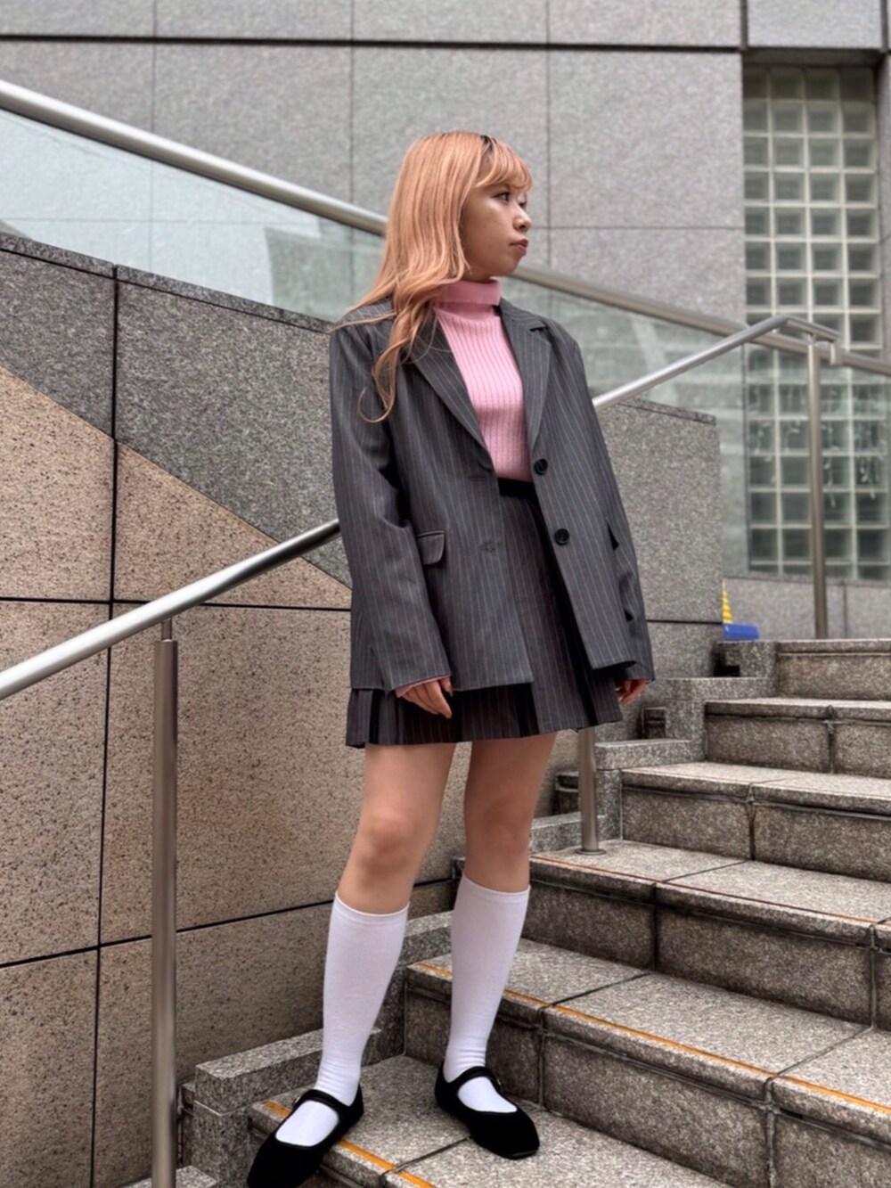 グレー系のテーラードジャケット、グレー系のスカート、ピンク系のニット/セーターを着用したレディースの秋コーディネートの2枚目の写真