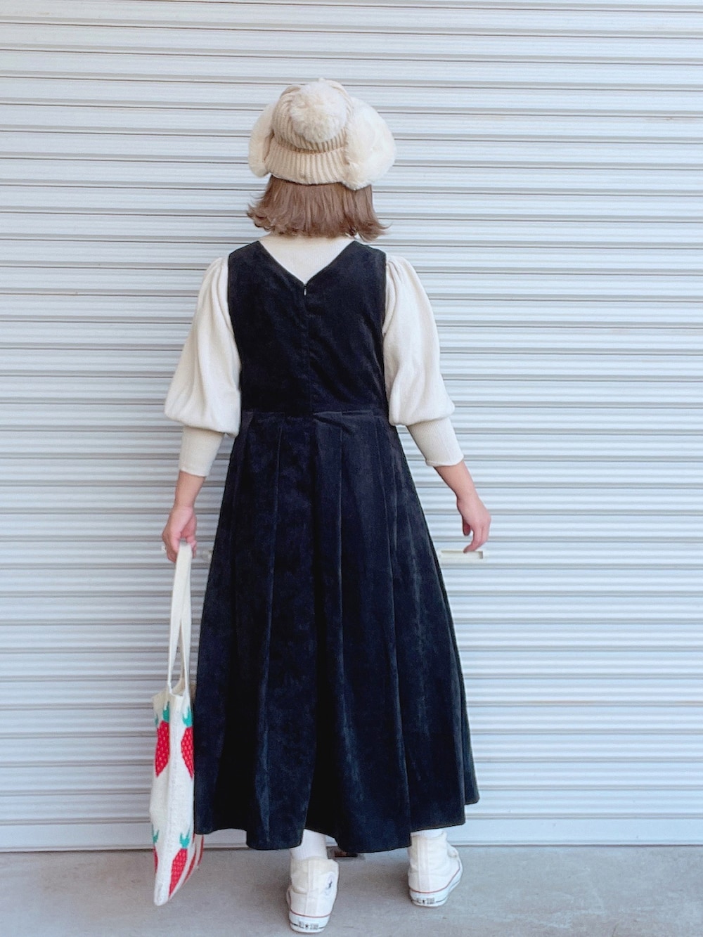 ブラック系のジャンパースカート、ホワイト系のニット/セーター、ホワイト系のトートバッグを着用したレディースの秋コーディネートの2枚目の写真