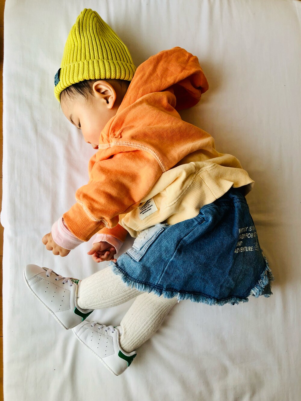 オレンジ系のパーカー、ブルー系のスカート、ホワイト系のスニーカーを着用したキッズの春コーディネートの2枚目の写真