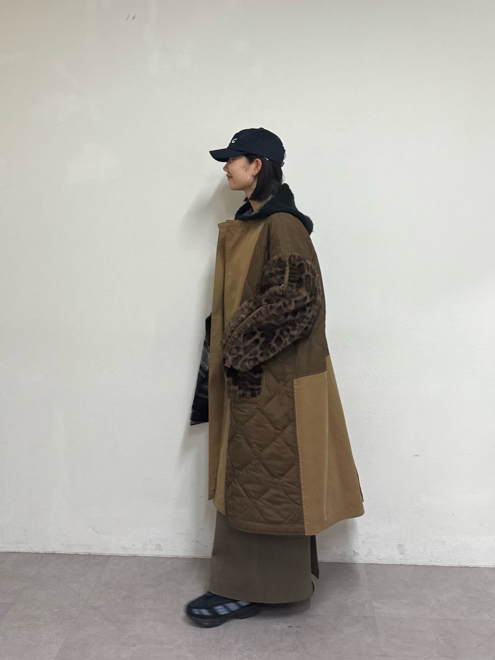 ブラウン系のノーカラーコート、グリーン系のスカート、ブラック系のパーカーを着用したレディースの秋コーディネートの2枚目の写真