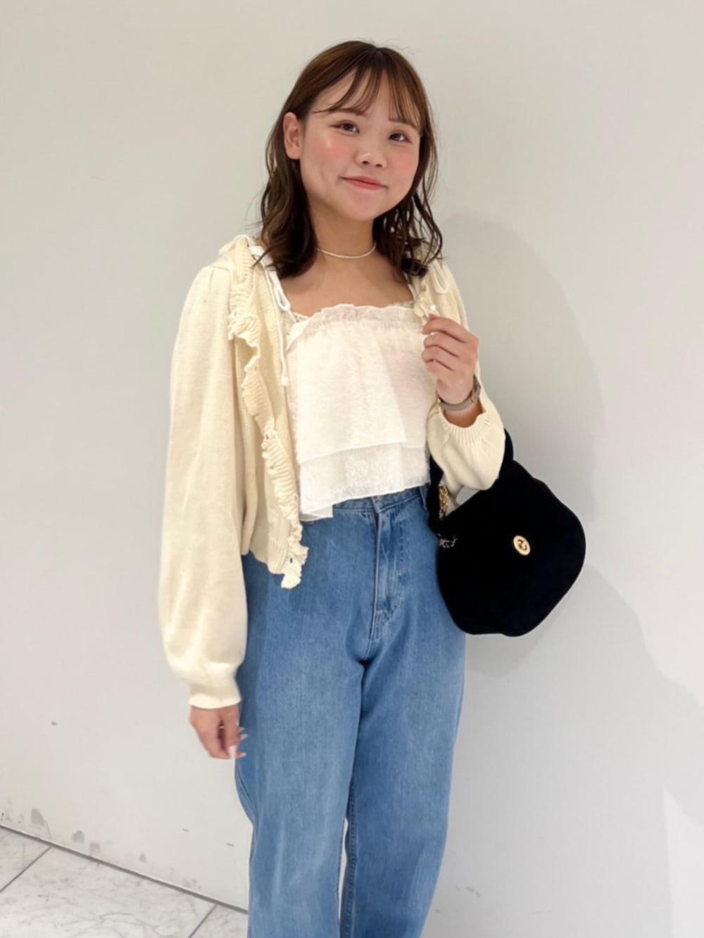 ブルー系のデニムパンツ、ブラック系のショルダーバッグ、ホワイト系のキャミソールを着用したレディースの秋コーディネートの2枚目の写真