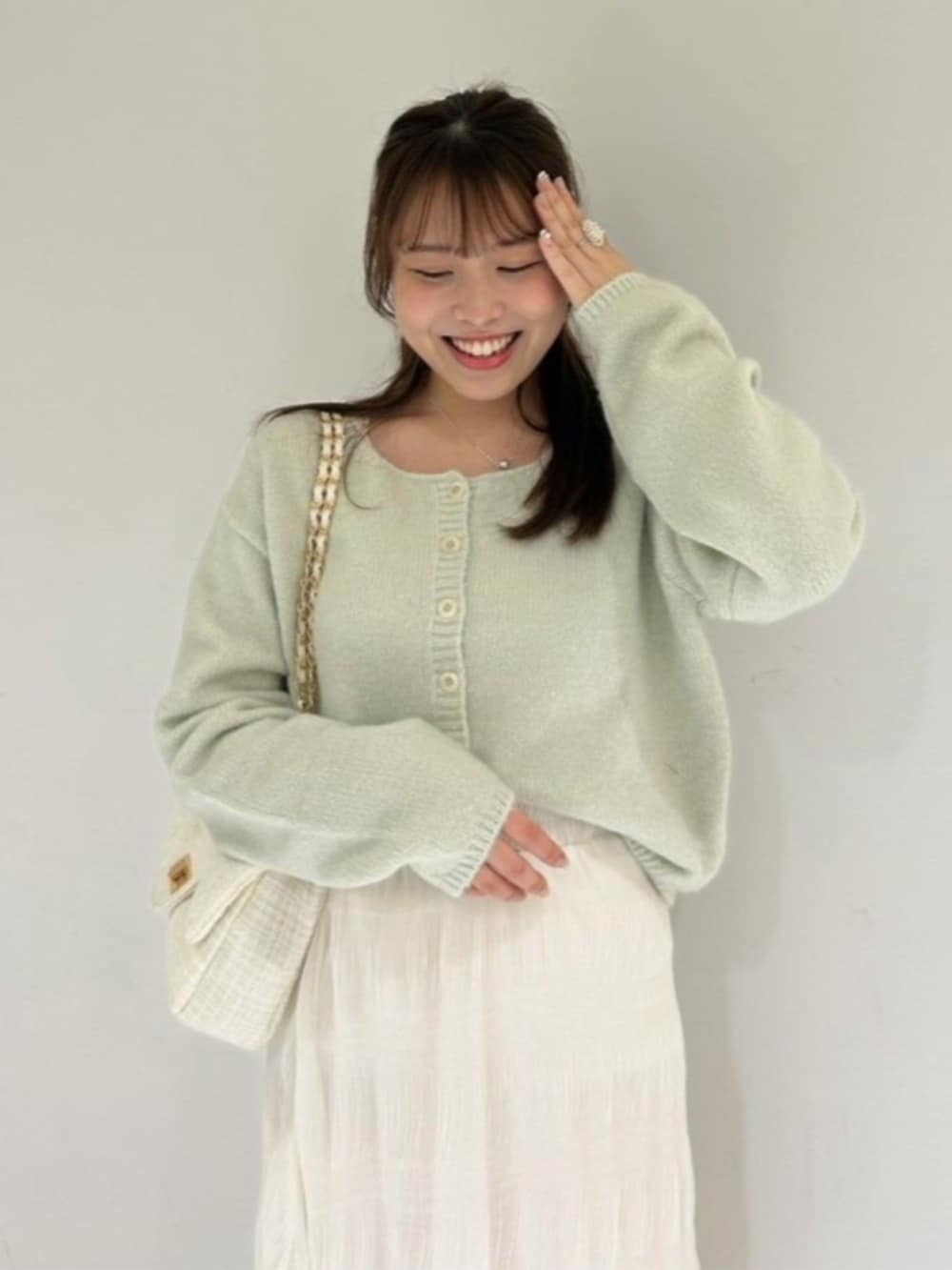 ホワイト系のショルダーバッグ、ホワイト系のスカート、グリーン系のカーディガン/ボレロを着用したレディースの冬コーディネートの2枚目の写真