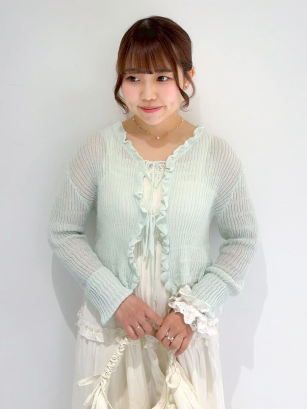 ホワイト系のショルダーバッグ、ホワイト系のワンピース、グリーン系のカーディガン/ボレロを着用したレディースの春コーディネートの2枚目の写真