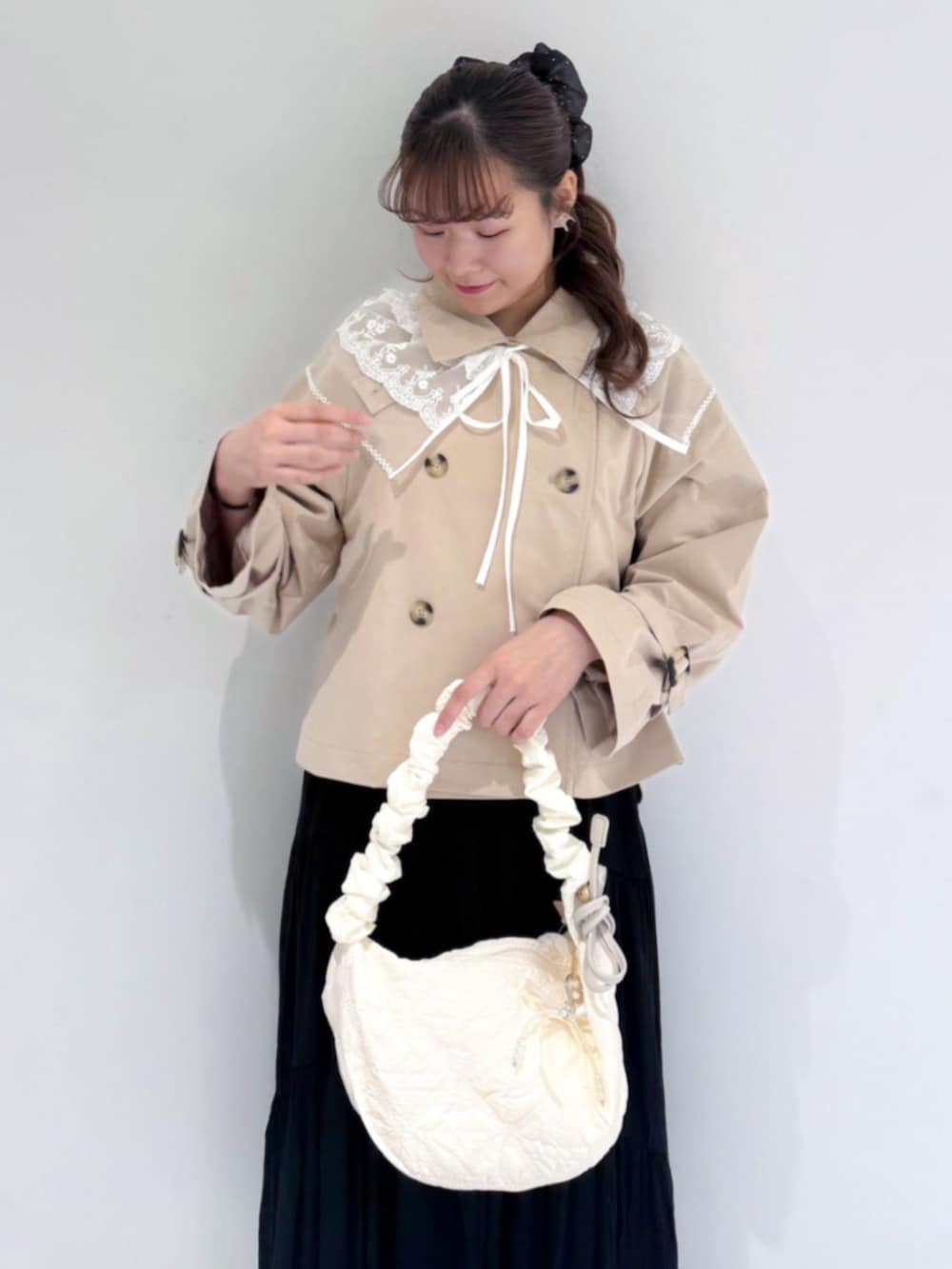ホワイト系のショルダーバッグ、ベージュ系のトレンチコート、ホワイト系のスカートを着用したレディースの春コーディネートの2枚目の写真