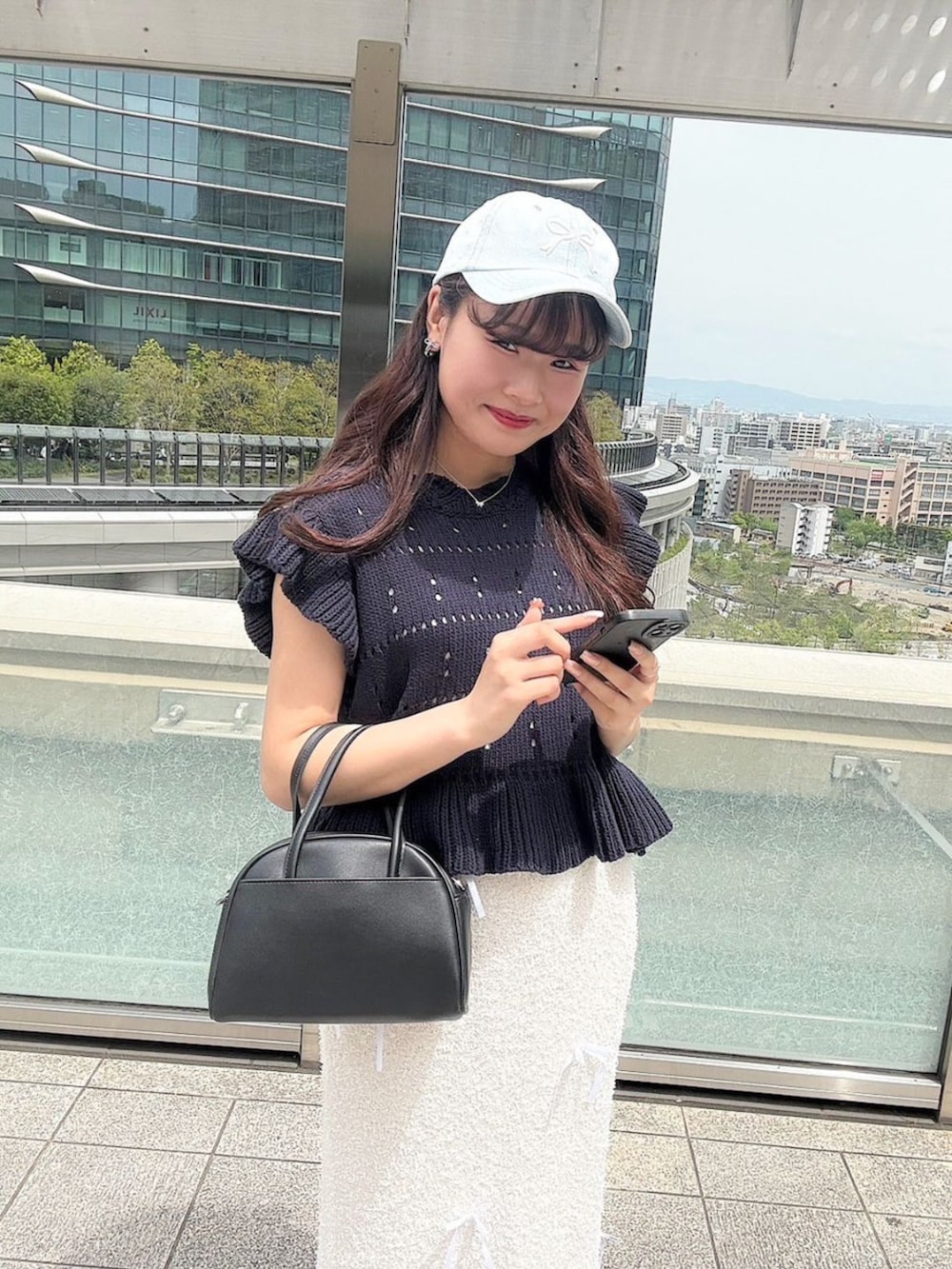 ブラック系のハンドバッグ、ブルー系のニット/セーター、ホワイト系のスカートを着用したレディースの春コーディネートの2枚目の写真