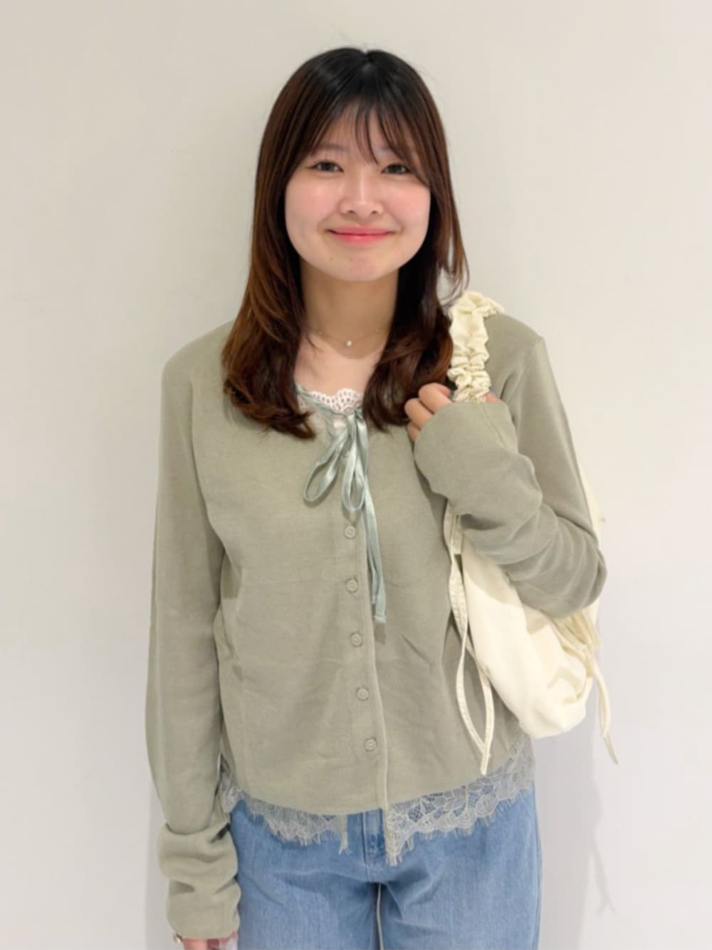 ブルー系のデニムパンツ、ホワイト系のショルダーバッグ、グリーン系のカーディガン/ボレロを着用したレディースの夏コーディネートの2枚目の写真