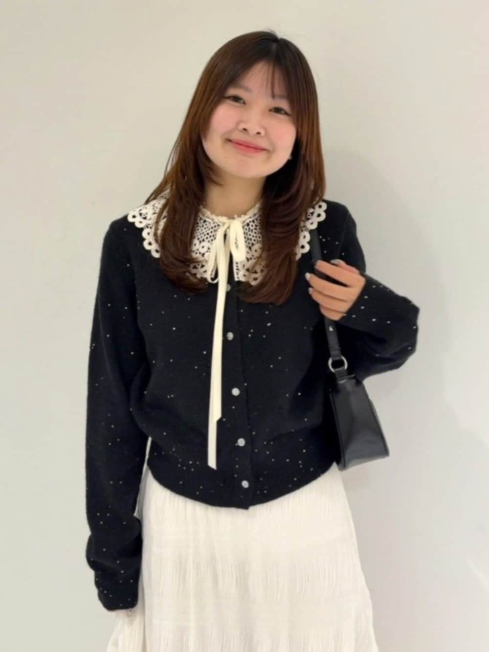 ブラック系のショルダーバッグ、ブラック系のニット/セーター、ホワイト系のスカートを着用したレディースの冬コーディネートの2枚目の写真