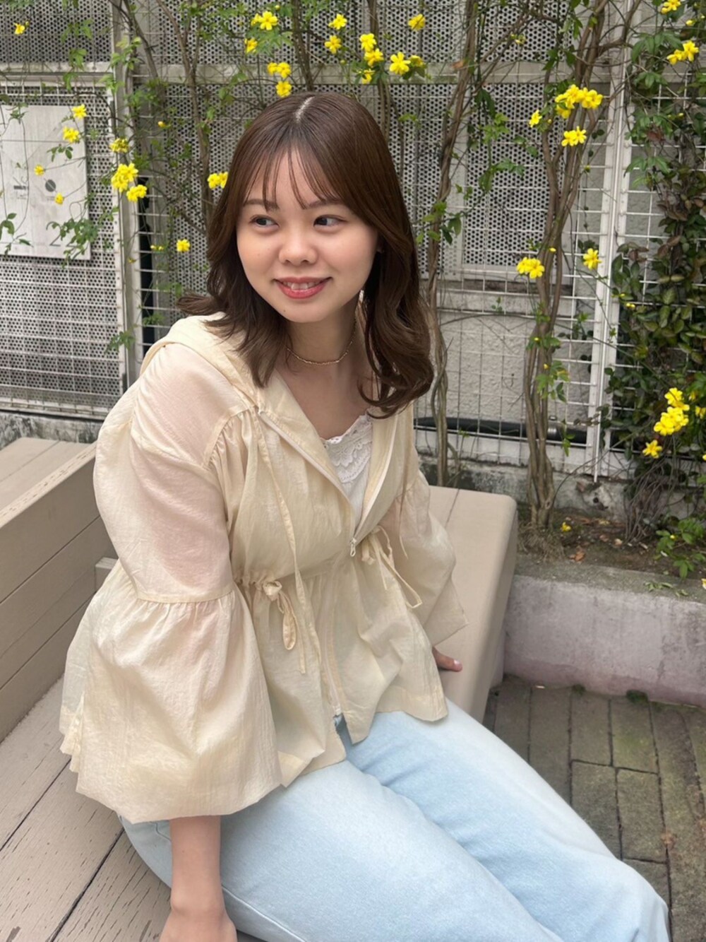 ホワイト系のキャミソール、ベージュ系のナイロンジャケット、ブルー系のデニムパンツを着用したレディースの春コーディネートの3枚目の写真