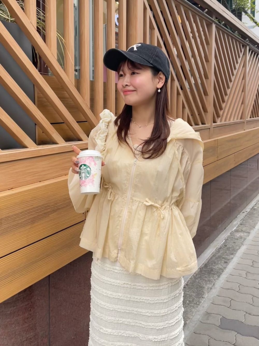 ベージュ系のナイロンジャケット、ホワイト系のスカート、ブラック系のキャップを着用したレディースの春コーディネートの2枚目の写真