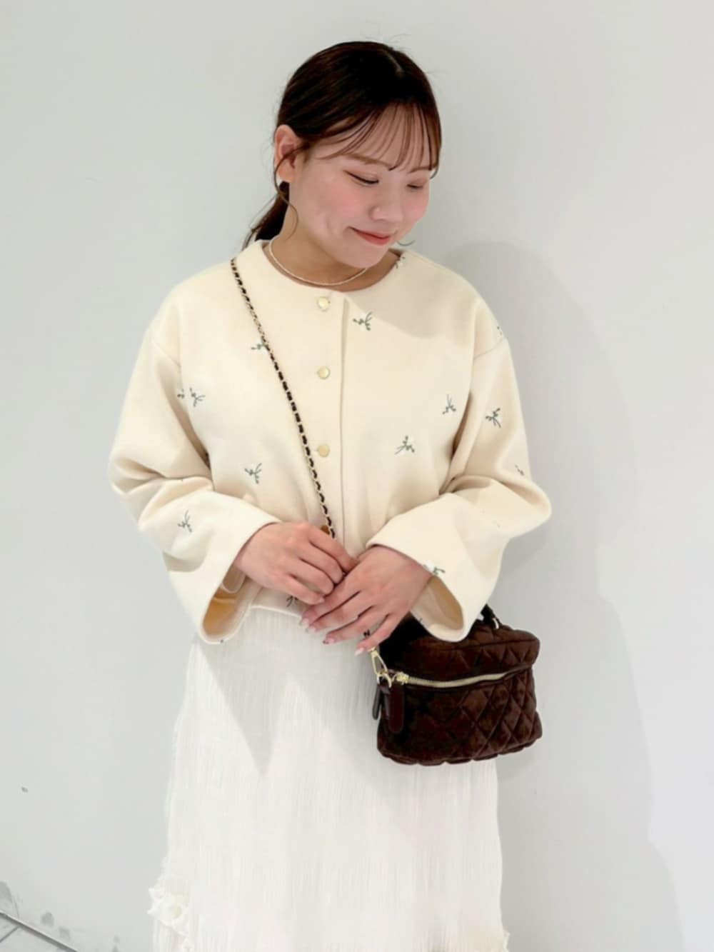 ブラウン系のショルダーバッグ、ホワイト系のスカート、ホワイト系のノーカラージャケットを着用したレディースの冬コーディネートの2枚目の写真