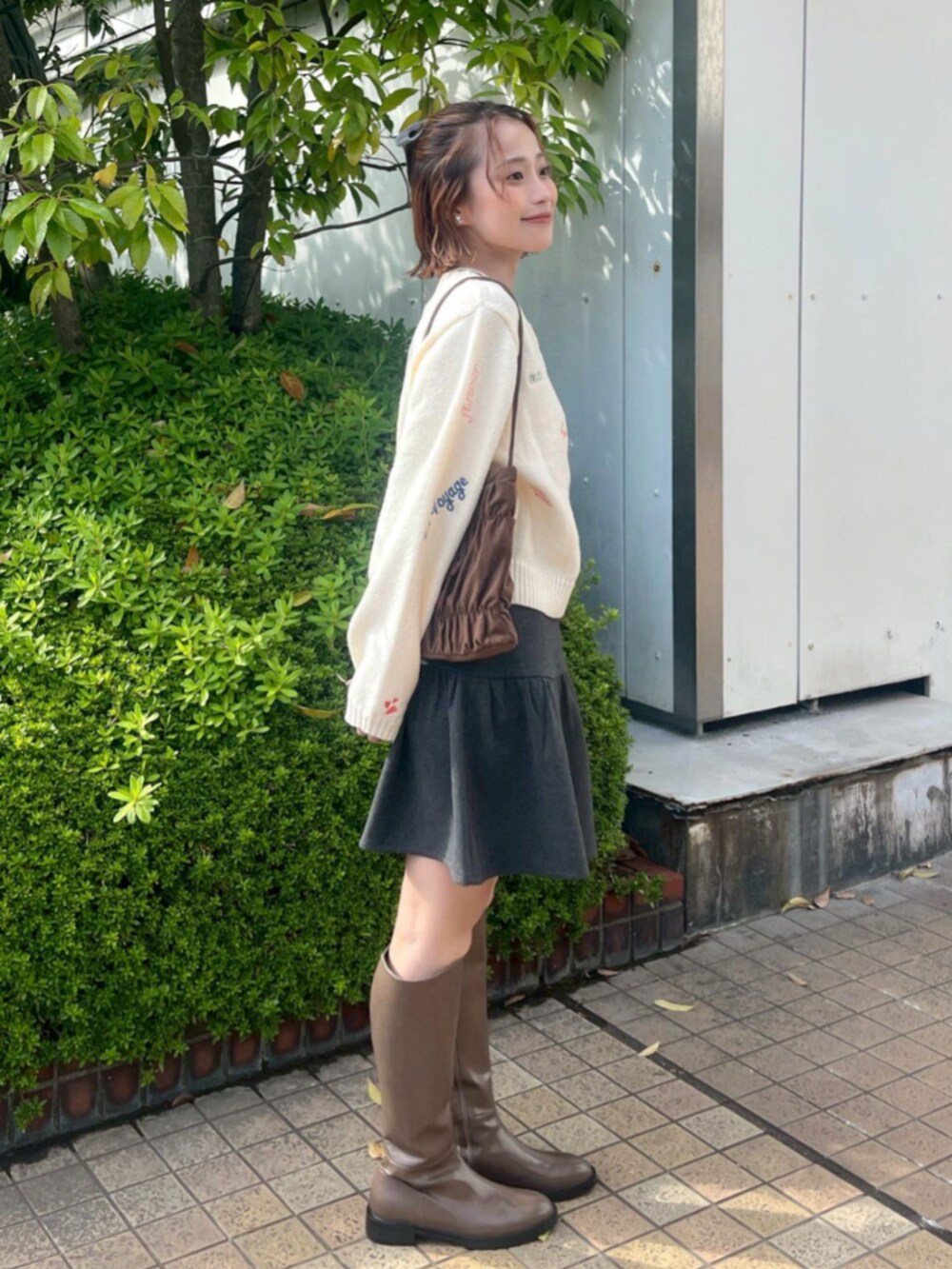 ブラウン系のショルダーバッグ、グレー系のスカート、ホワイト系のノーカラーコートを着用したレディースの秋コーディネートの2枚目の写真