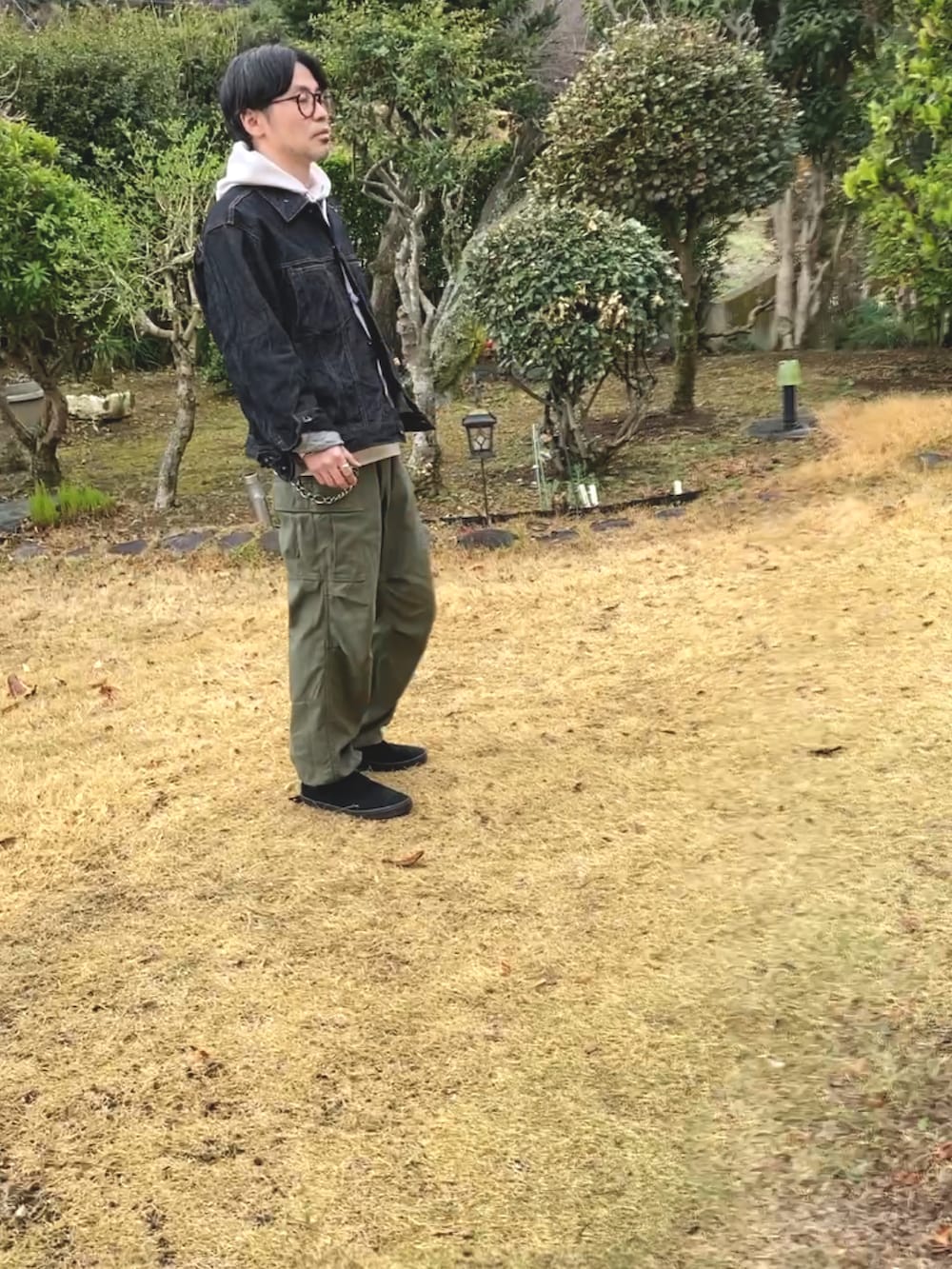 ベージュ系のパーカー、ブラック系のデニムジャケット、グリーン系のカーゴパンツを着用したメンズの春コーディネートの3枚目の写真