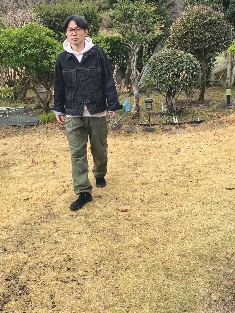 ベージュ系のパーカー、ブラック系のデニムジャケット、グリーン系のカーゴパンツを着用したメンズの春コーディネートの2枚目の写真