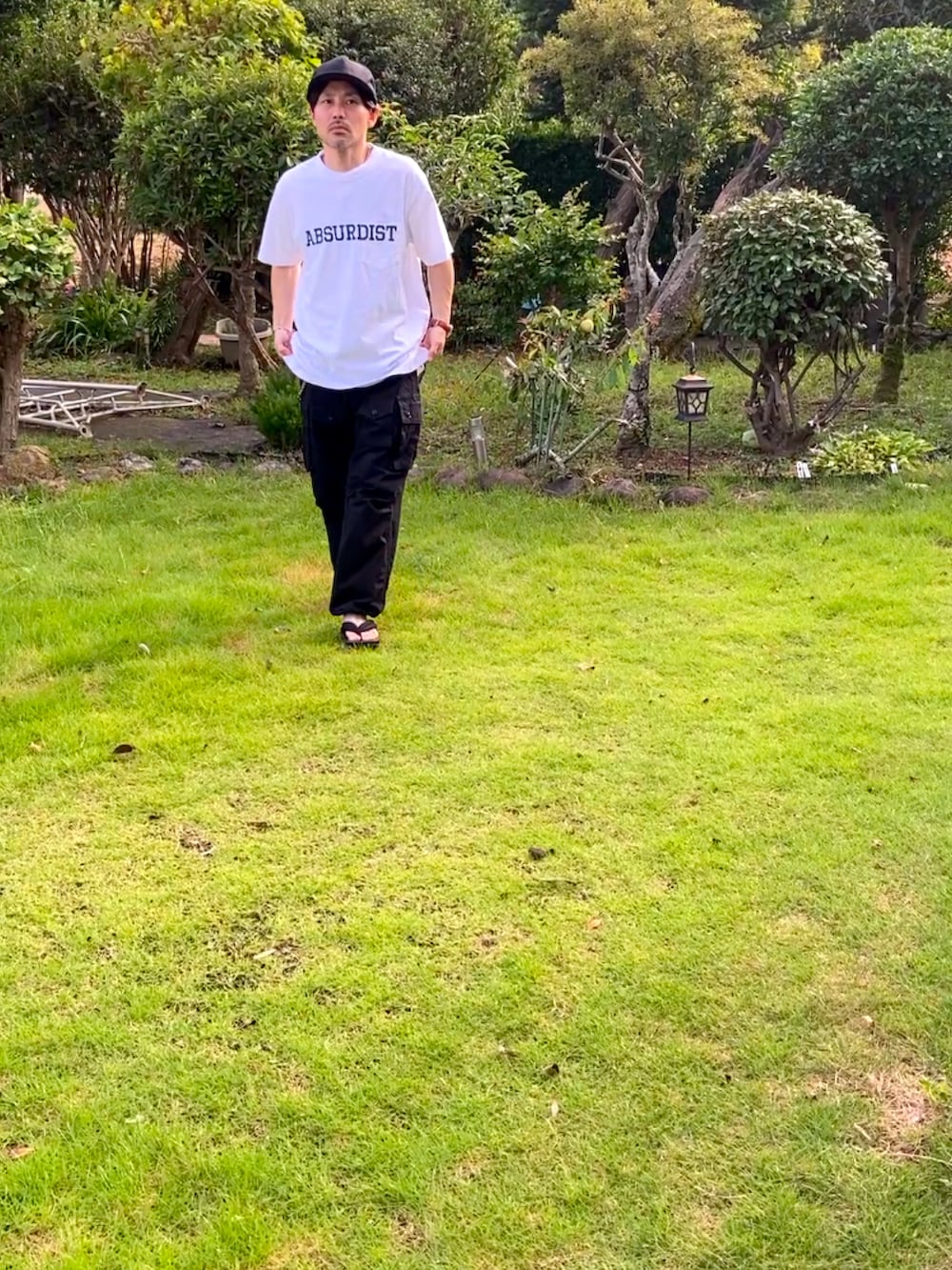 ホワイト系のTシャツ/カットソー、ブラック系のカーゴパンツ、ブラック系のサンダルを着用したメンズの夏コーディネートの2枚目の写真