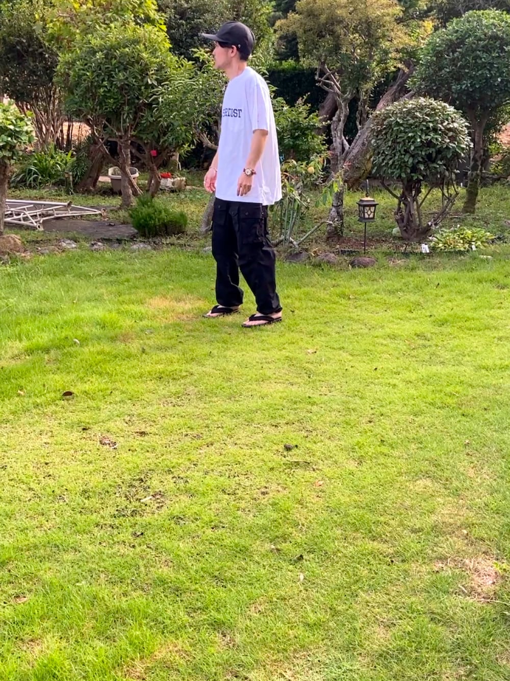 ホワイト系のTシャツ/カットソー、ブラック系のカーゴパンツ、ブラック系のサンダルを着用したメンズの夏コーディネートの3枚目の写真