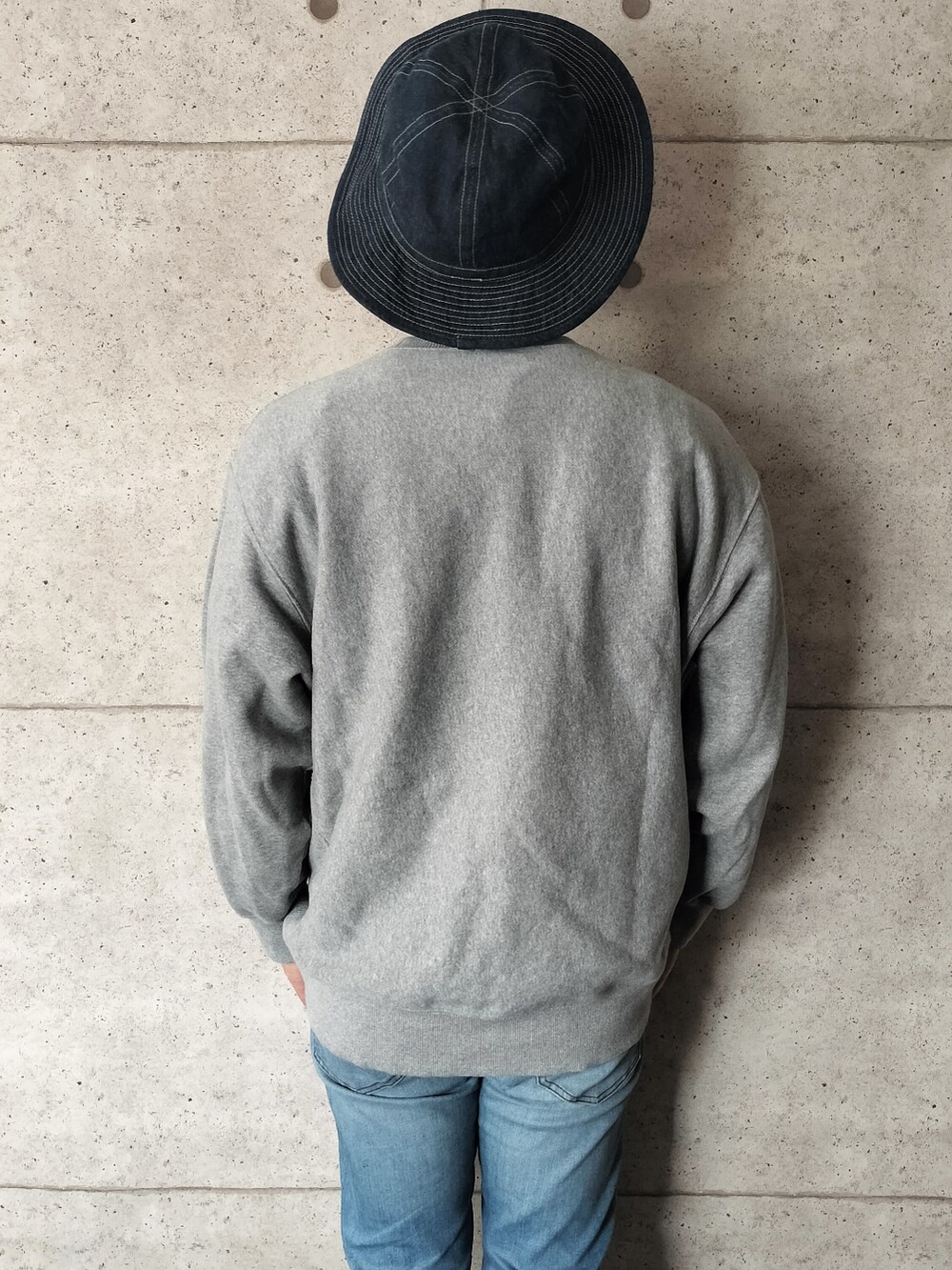 グレー系のスウェット、ブルー系のデニムパンツ、ブルー系のハットを着用したメンズの秋コーディネートの2枚目の写真