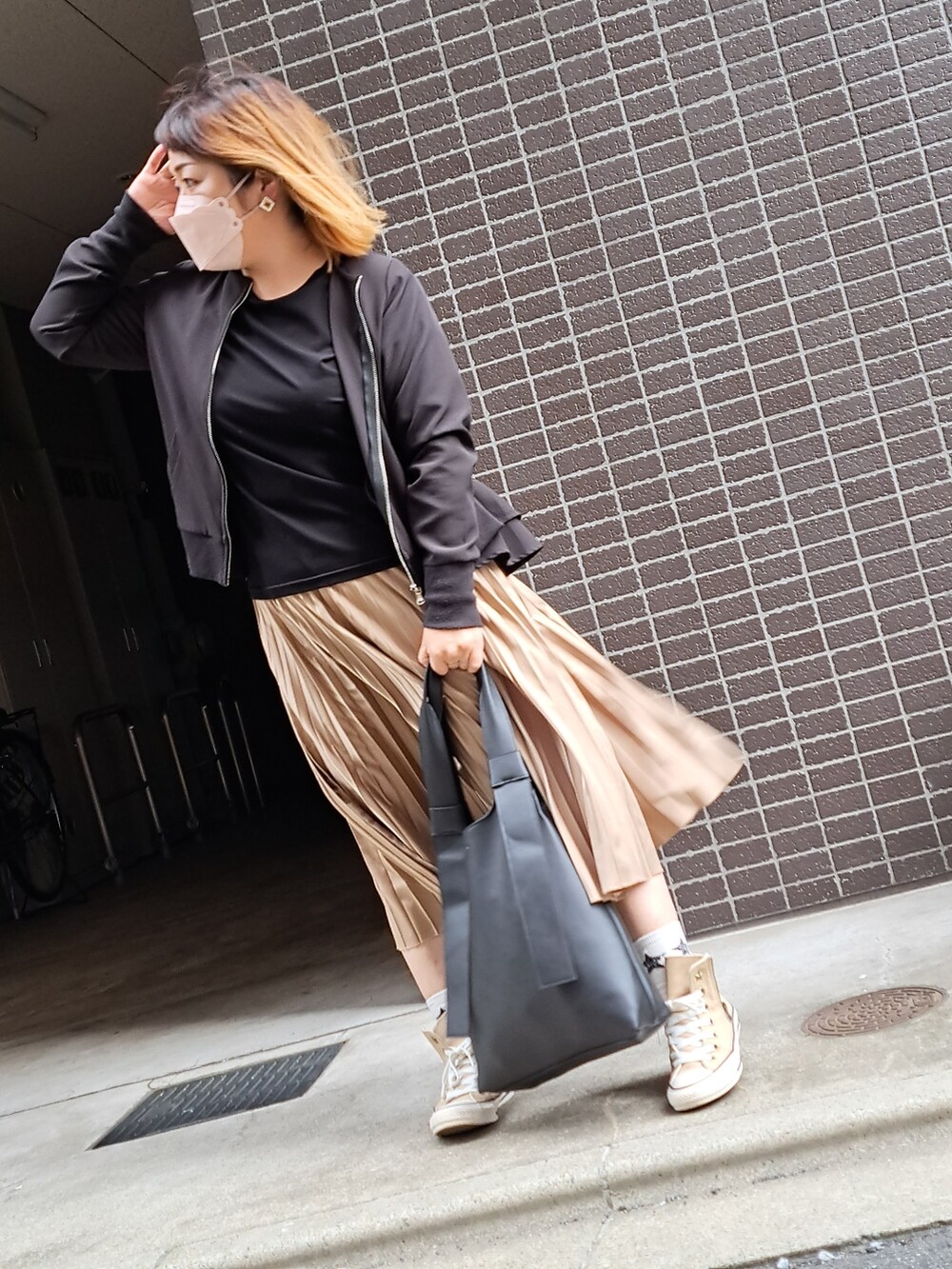 ブラック系のノーカラーコート、ゴールド系のスカート、ベージュ系のスニーカーを着用したレディースの秋コーディネートの2枚目の写真