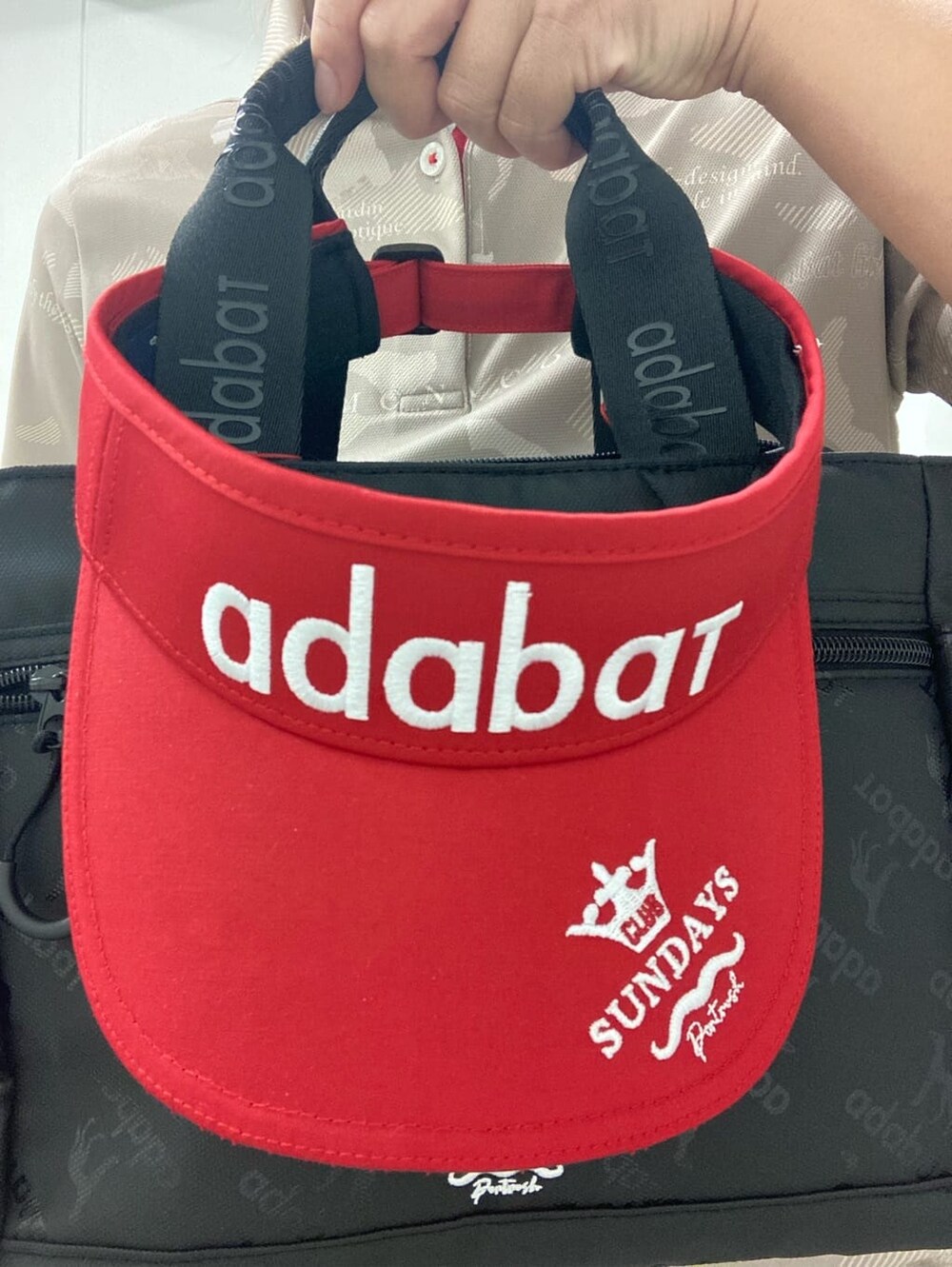 ベージュ系のポロシャツ、ブラック系のハンドバッグ、レッド系のサンバイザーを着用したレディースの夏コーディネートの7枚目の写真