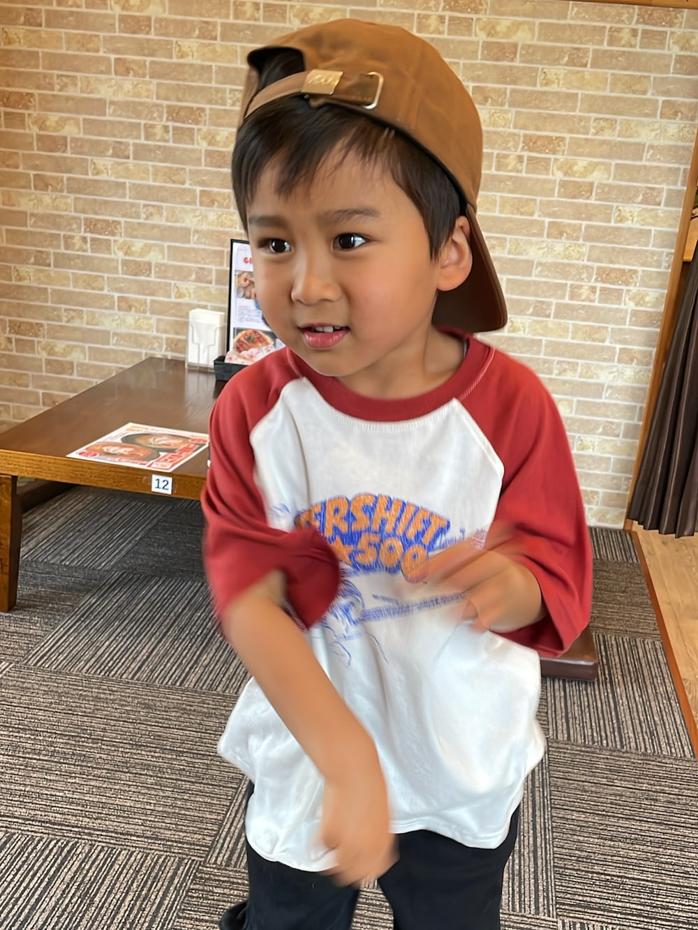 レッド系のTシャツ/カットソー、ブラック系のチノパンツ、ブラウン系のキャップを着用したキッズの春コーディネートの2枚目の写真