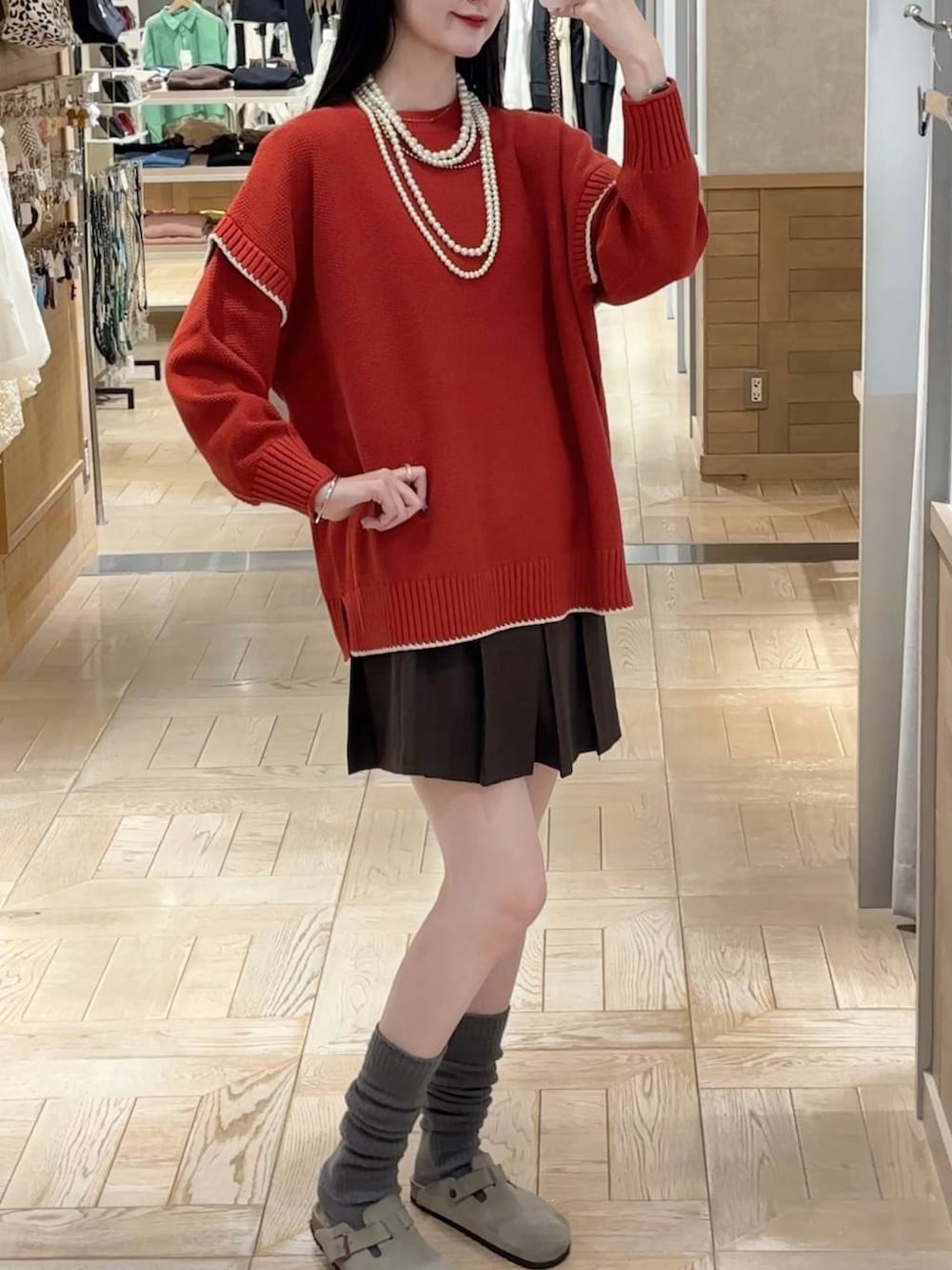 レッド系のニット/セーター、ブラウン系のスカート、ベージュ系のネックレスを着用したレディースの秋コーディネートの2枚目の写真
