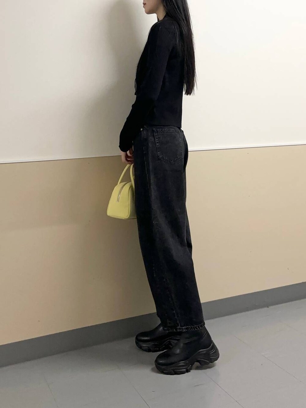 ブラック系のデニムパンツ、ブラック系のブーツ、イエロー系のボストンバッグを着用したレディースの秋コーディネートの2枚目の写真