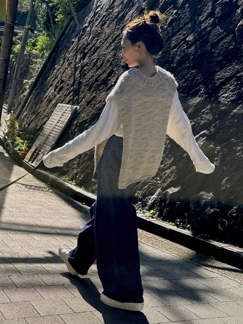 ブラック系のデニムパンツ、ホワイト系のスニーカー、ベージュ系のベストを着用したレディースの秋コーディネートの2枚目の写真