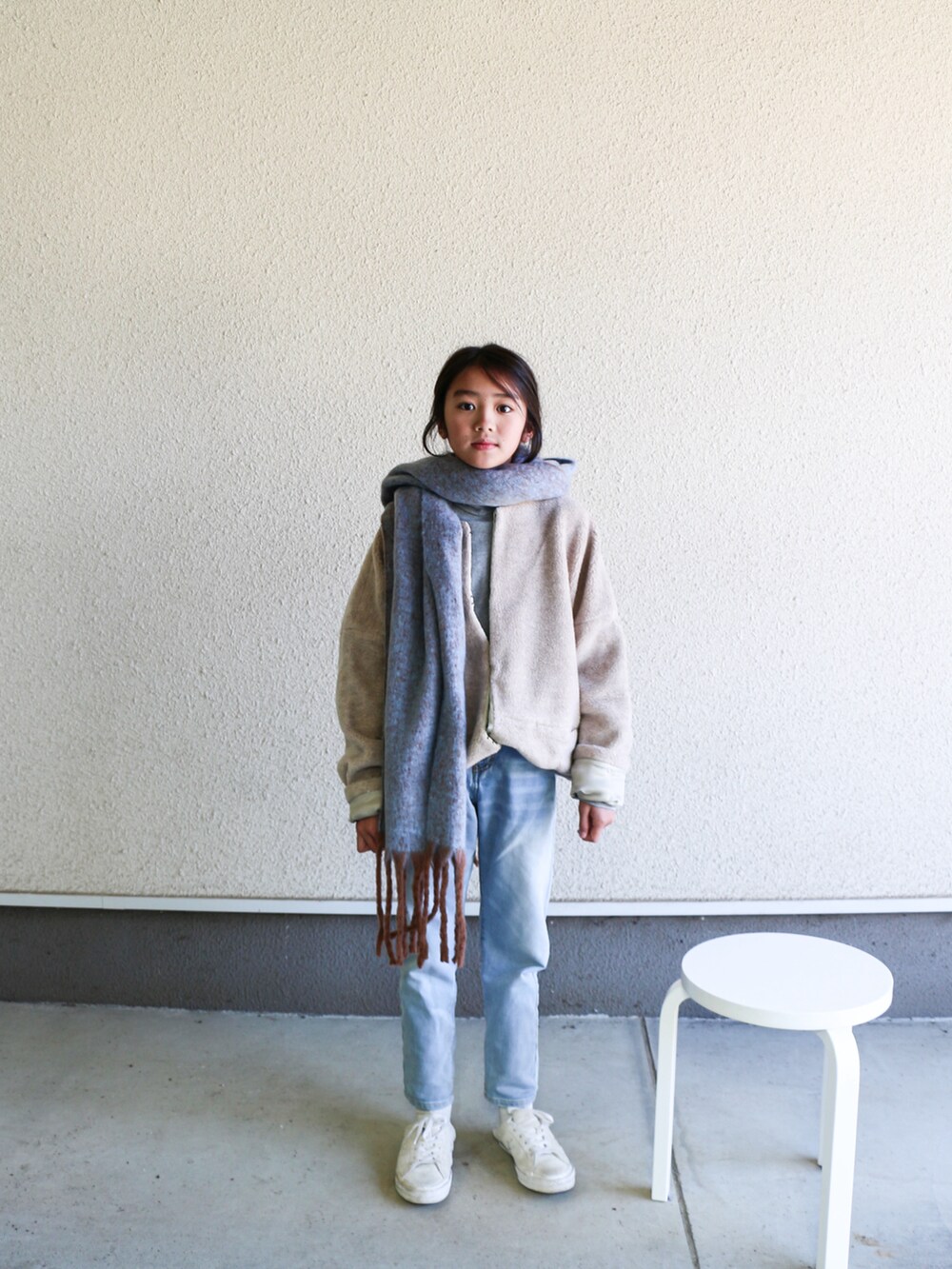 ベージュ系のノーカラージャケット、ホワイト系のスニーカー、ブルー系のデニムパンツを着用したキッズの冬コーディネートの3枚目の写真