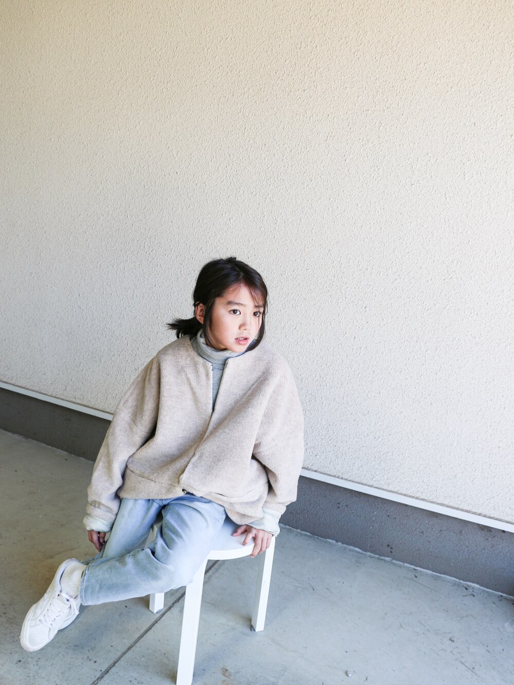 ベージュ系のノーカラージャケット、ホワイト系のスニーカー、ブルー系のデニムパンツを着用したキッズの冬コーディネートの2枚目の写真