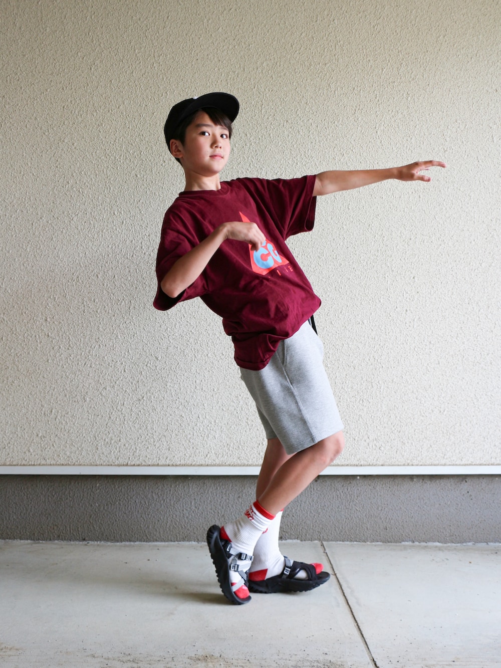 レッド系のTシャツ/カットソー、グレー系のパンツ、ブラック系のサンダルを着用したキッズの春コーディネートの2枚目の写真