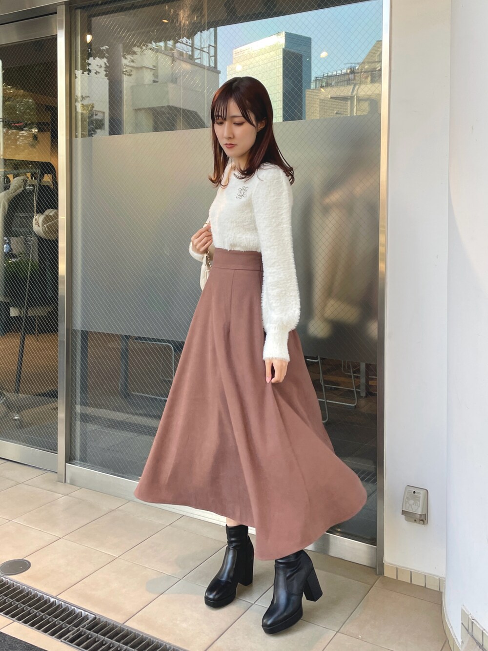ホワイト系のニット/セーター、ホワイト系のショルダーバッグ、ブラウン系のスカートを着用したレディースの冬コーディネートの2枚目の写真