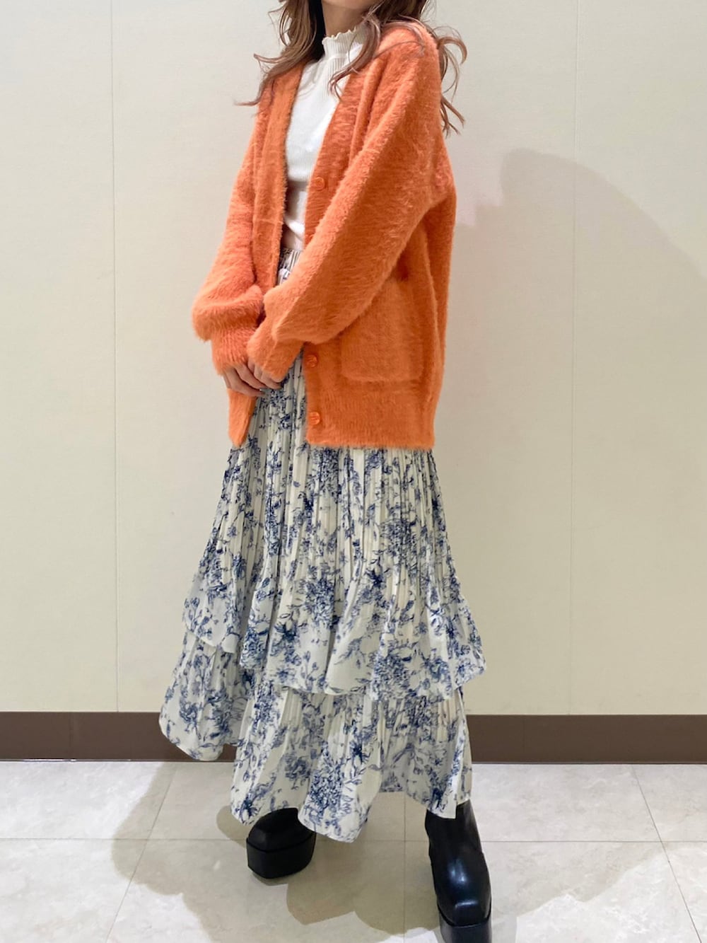 オレンジ系のカーディガン/ボレロ、ブルー系のスカートを着用したレディースの冬コーディネートの2枚目の写真