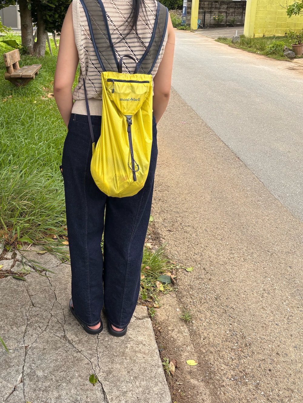 ブルー系のデニムパンツ、ブラック系のサンダル、イエロー系のバックパック/リュックを着用したレディースの夏コーディネートの2枚目の写真