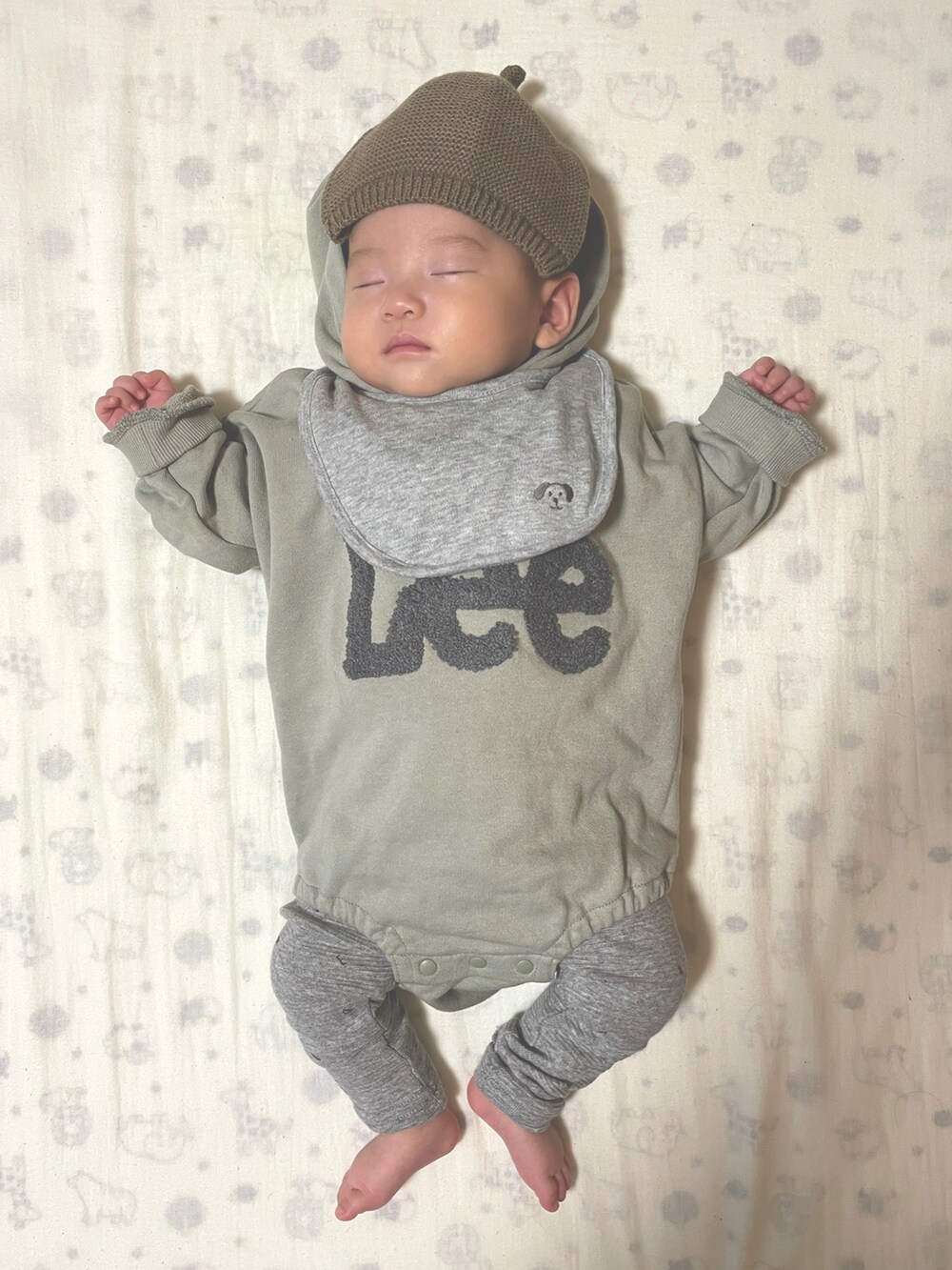 グリーン系のロンパース、グレー系のスタイ/よだれかけ、グリーン系の帽子を着用したキッズの冬コーディネートの2枚目の写真