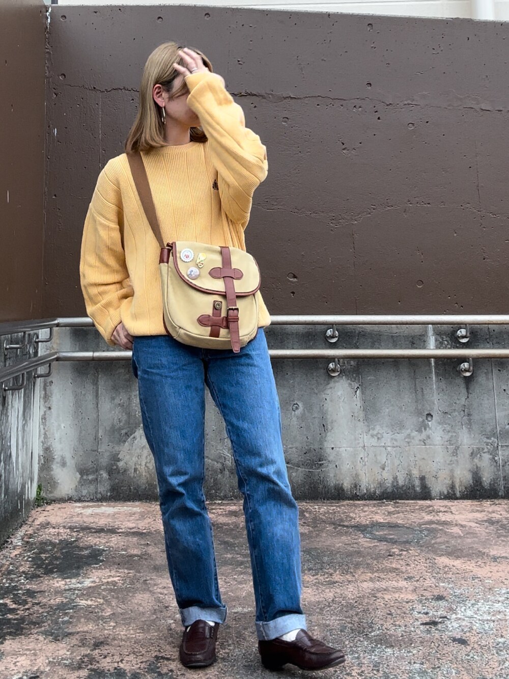 イエロー系のニット/セーター、ブルー系のデニムパンツ、ベージュ系のショルダーバッグを着用したレディースの春コーディネートの2枚目の写真