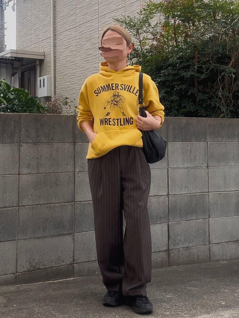 イエロー系のパーカー、ブラウン系のスラックス、ブラック系のショルダーバッグを着用したレディースの秋コーディネートの2枚目の写真