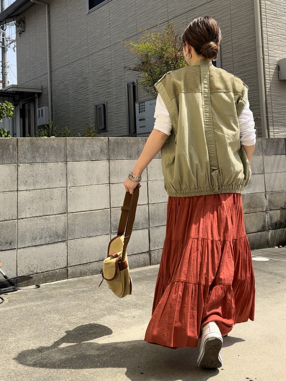 グリーン系のベスト、オレンジ系のスカート、ベージュ系のショルダーバッグを着用したレディースの春コーディネートの3枚目の写真
