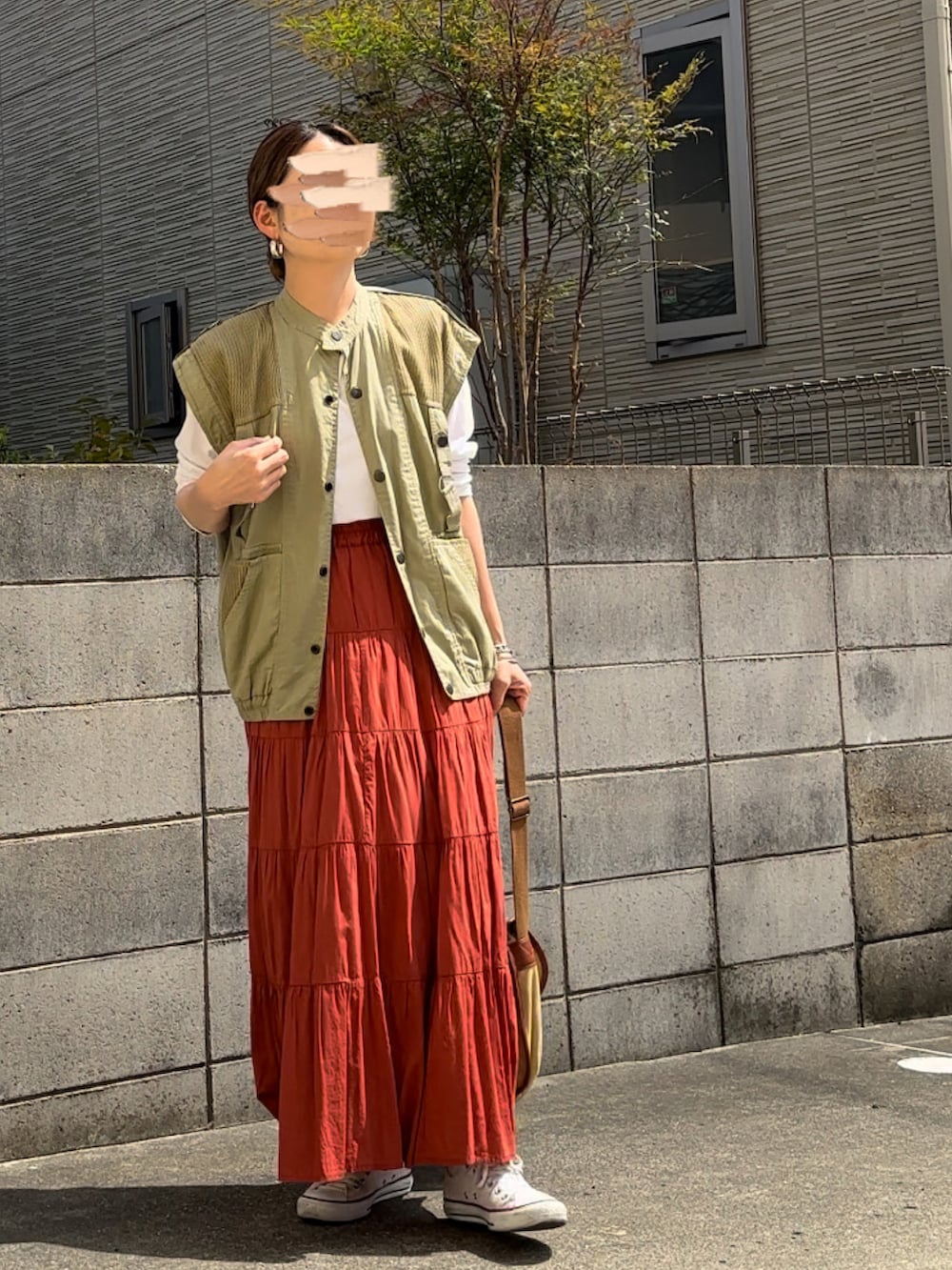 グリーン系のベスト、オレンジ系のスカート、ベージュ系のショルダーバッグを着用したレディースの春コーディネートの2枚目の写真