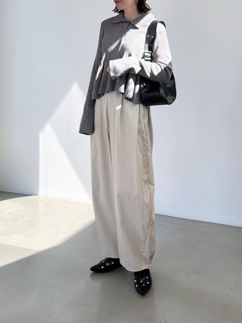 ホワイト系のチノパンツ、グレー系のカーディガン/ボレロ、ブラック系のハンドバッグを着用したレディースの春コーディネートの2枚目の写真