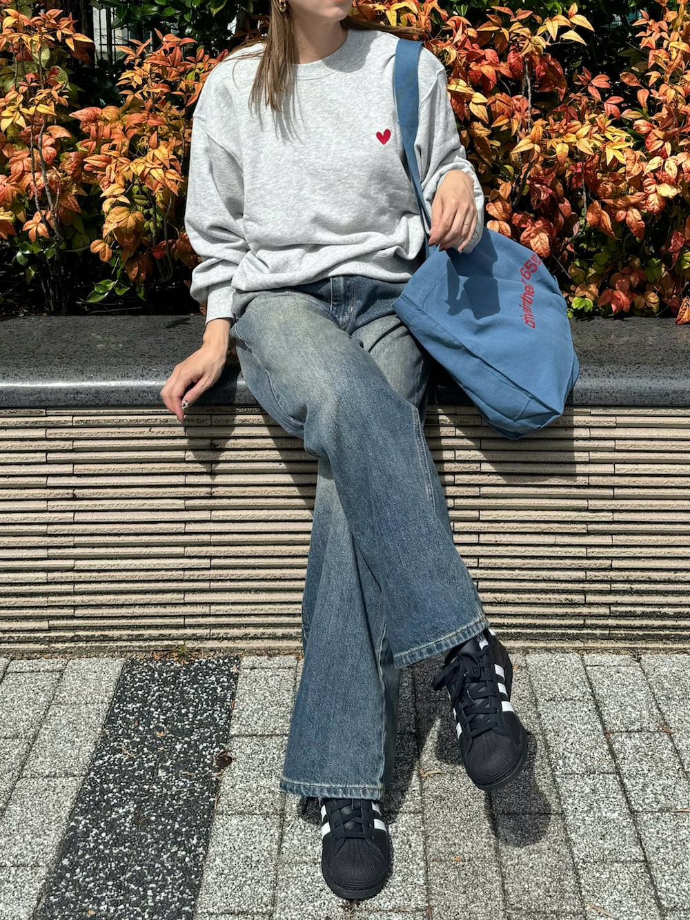 グレー系のスウェット、ブルー系のトートバッグ、ブルー系のデニムパンツを着用したレディースの秋コーディネートの2枚目の写真