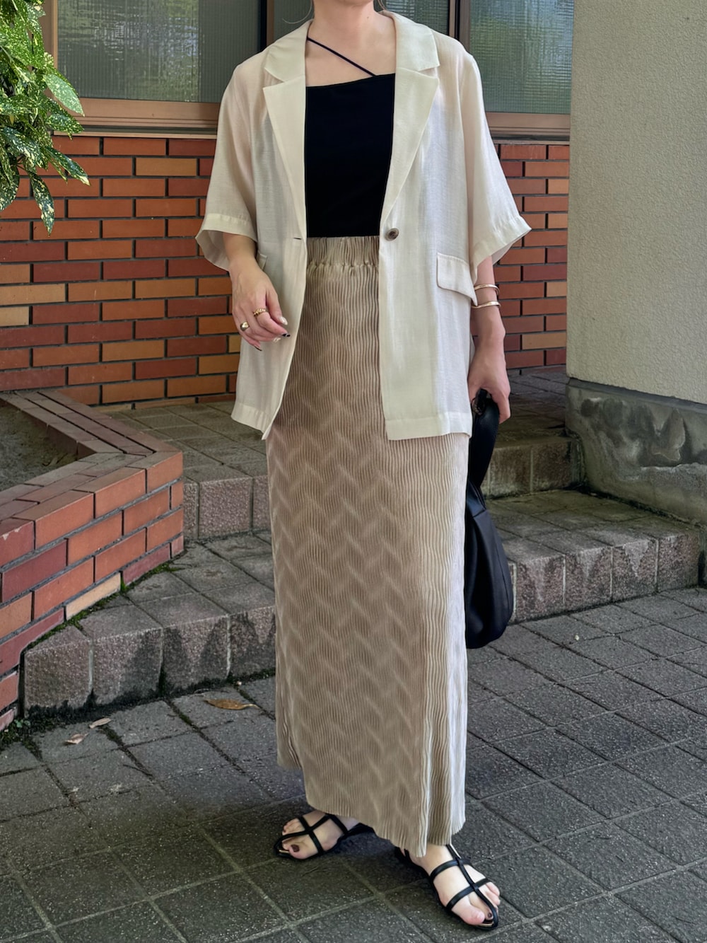 ホワイト系のテーラードジャケット、ブラック系のサンダル、ブラック系のハンドバッグを着用したレディースの夏コーディネートの4枚目の写真