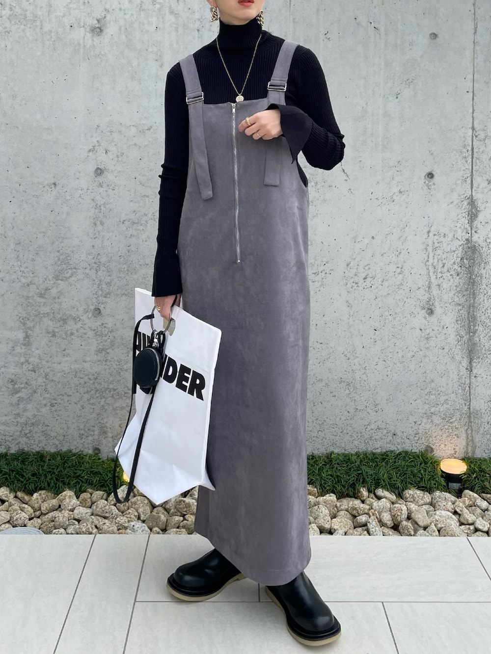 グレー系のジャンパースカート、ブラック系のニット/セーター、ブラック系のブーツを着用したレディースの秋コーディネートの2枚目の写真