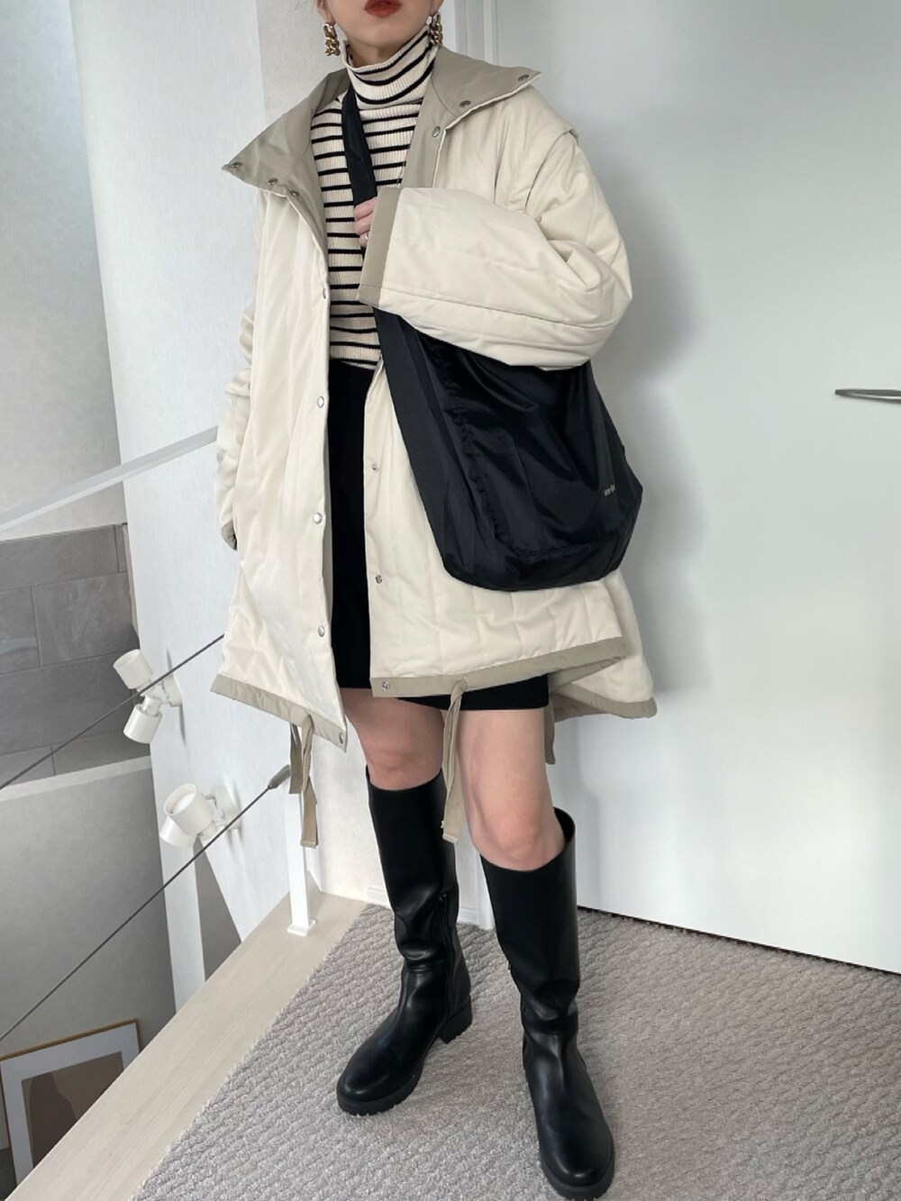 ブラック系のショルダーバッグ、ブラック系のニット/セーター、ホワイト系のダウンジャケット/コートを着用したレディースの冬コーディネートの2枚目の写真