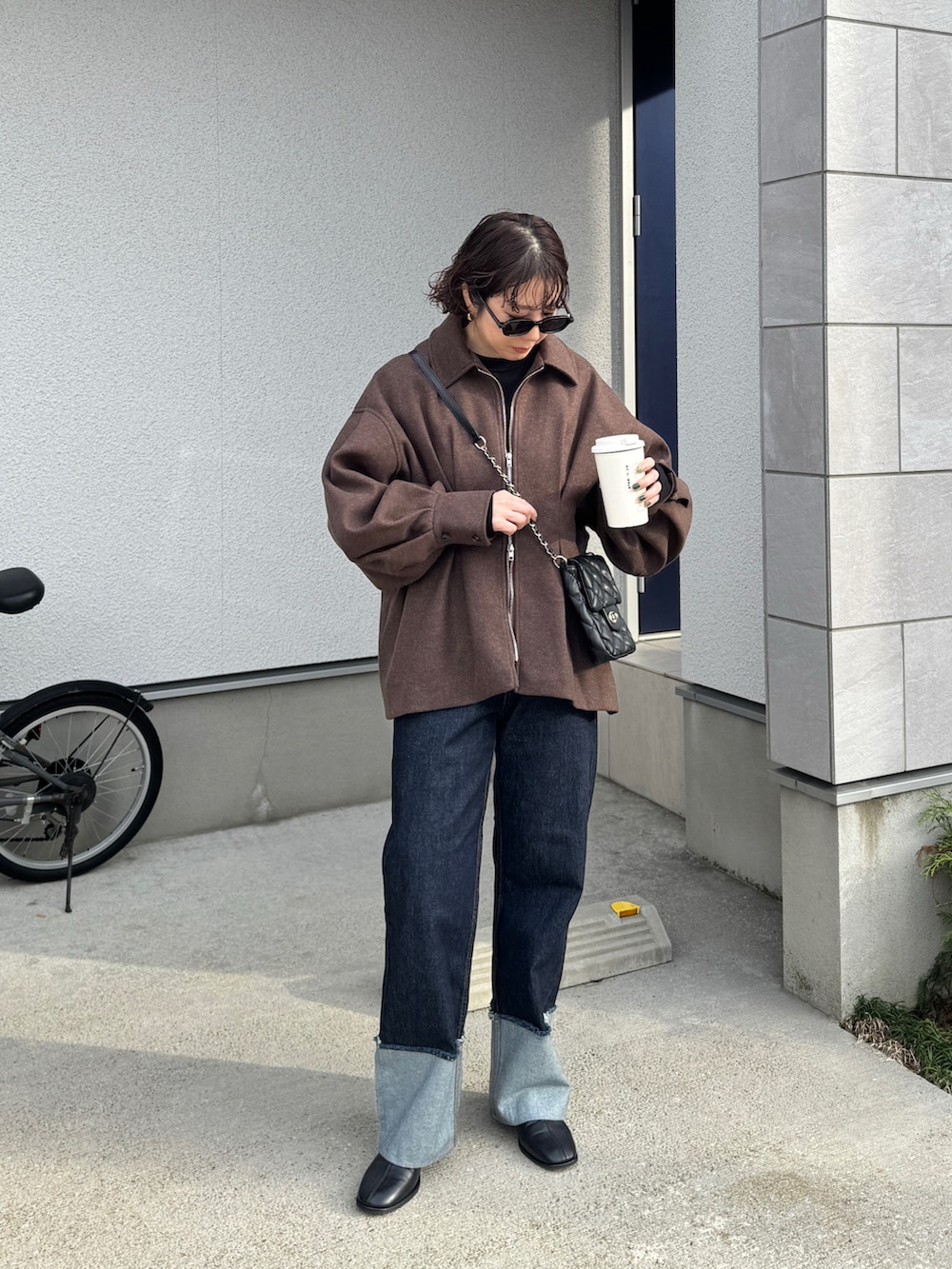 ブラウン系のブルゾン、ブルー系のデニムパンツ、ブラック系のショルダーバッグを着用したレディースの秋コーディネートの2枚目の写真