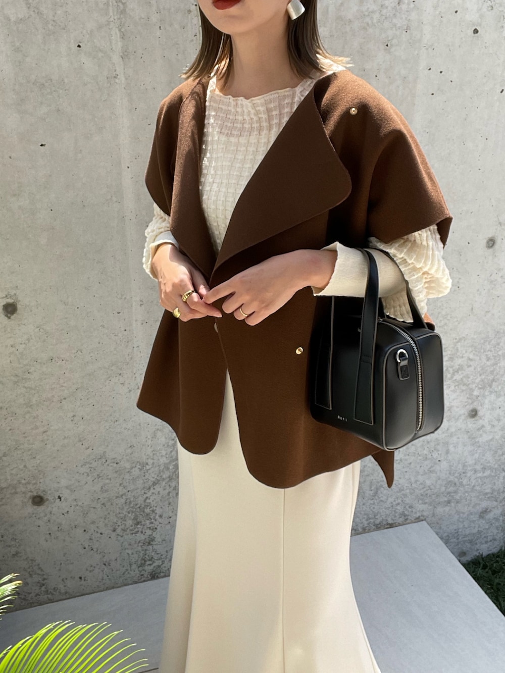 ブラウン系のベスト、ブラック系のボストンバッグ、ホワイト系のスカートを着用したレディースの夏コーディネートの4枚目の写真